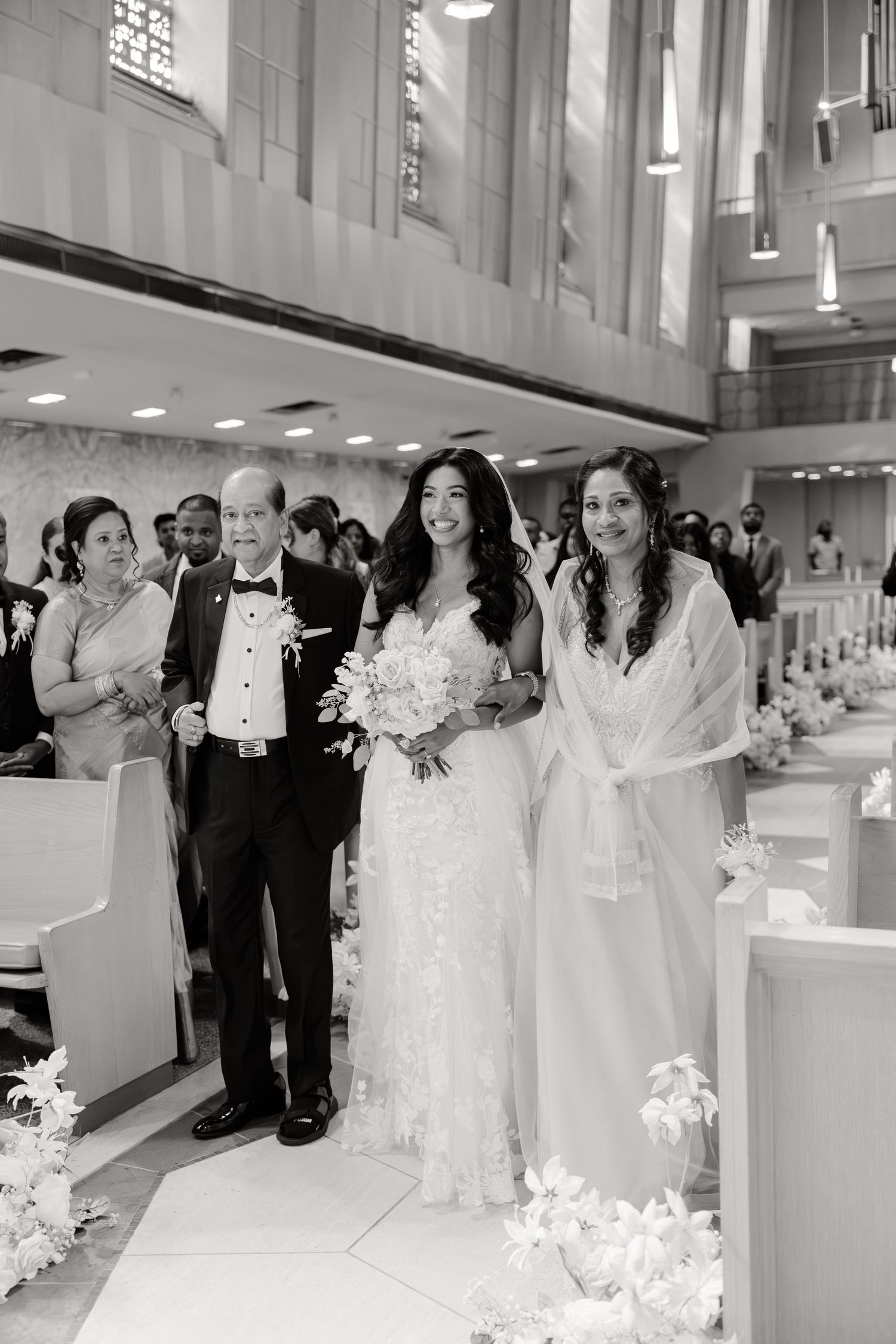 Wedding party proceeds down church aisle with bride in white gown and floral bouquet surrounded by loved ones.