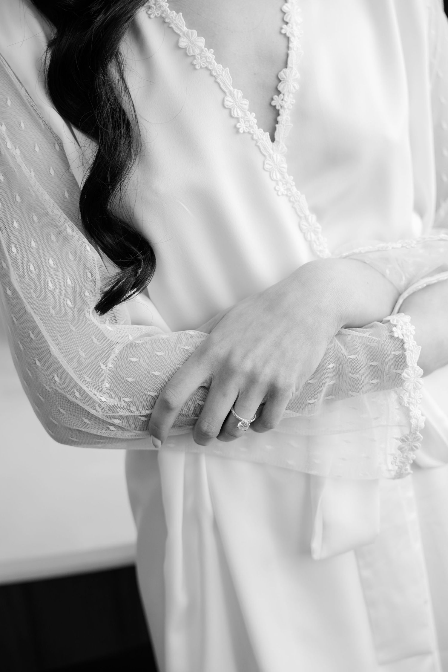 Close-up of delicate lace trim detail on white robe sleeve with ring on hand.
