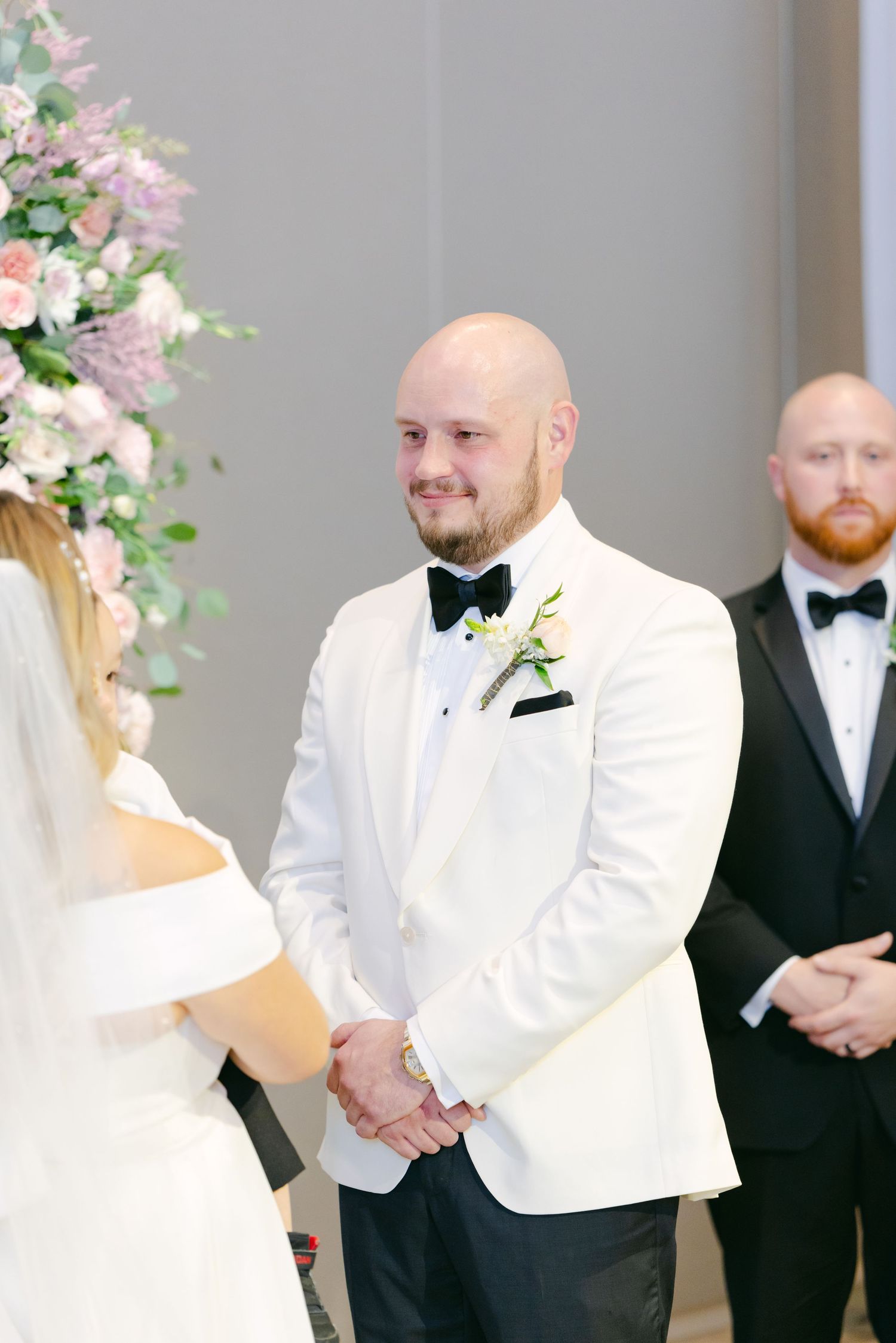 Groom in white dinner jacket stands at altar during wedding ceremony.