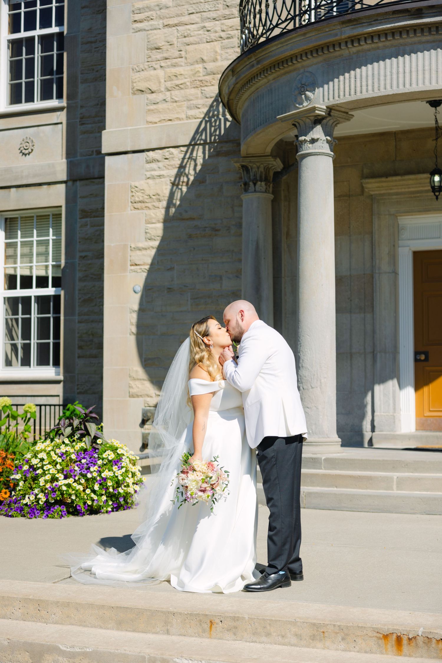 Couple shares romantic moment under limestone portico with ornate ironwork balcony.