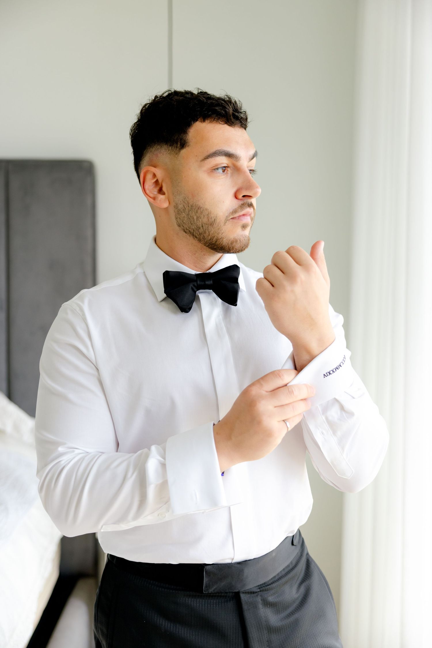 Person in crisp white shirt and bow tie adjusts sleeve near window.
