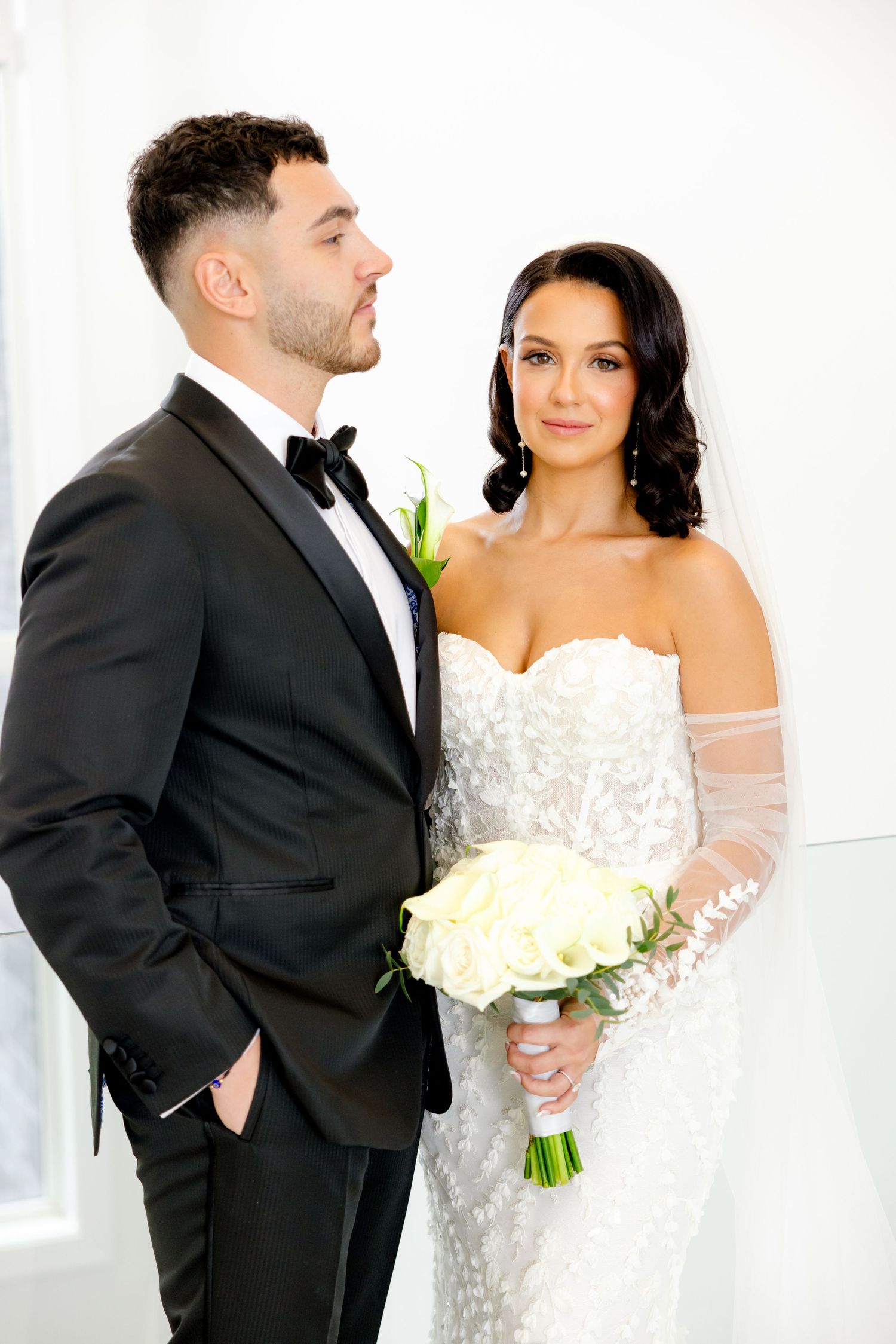 Wedding portrait with bride holding white bouquet and groom in classic black tuxedo.