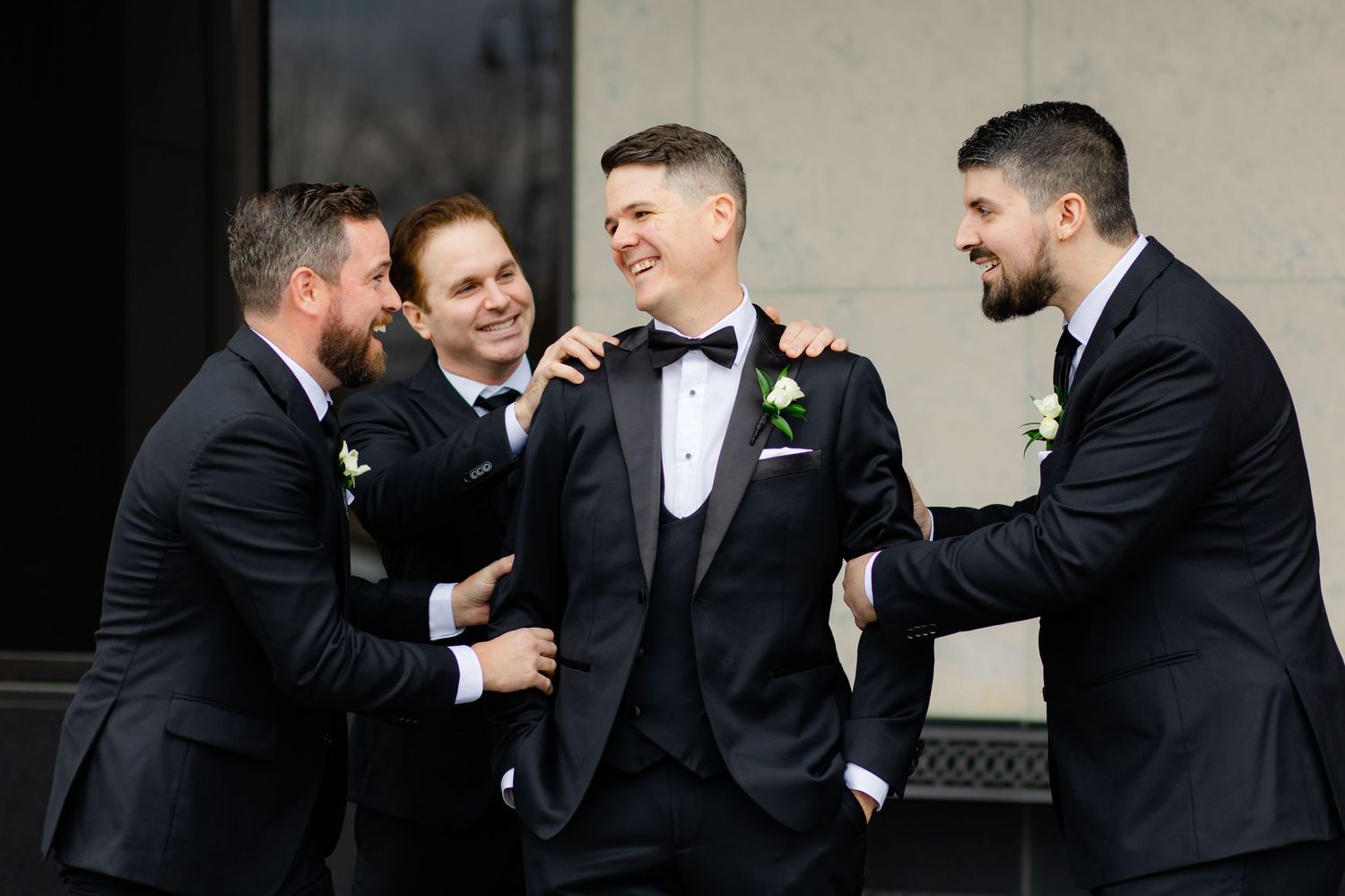 Groomsmen in black tuxedos share laughs during candid wedding photo moment.