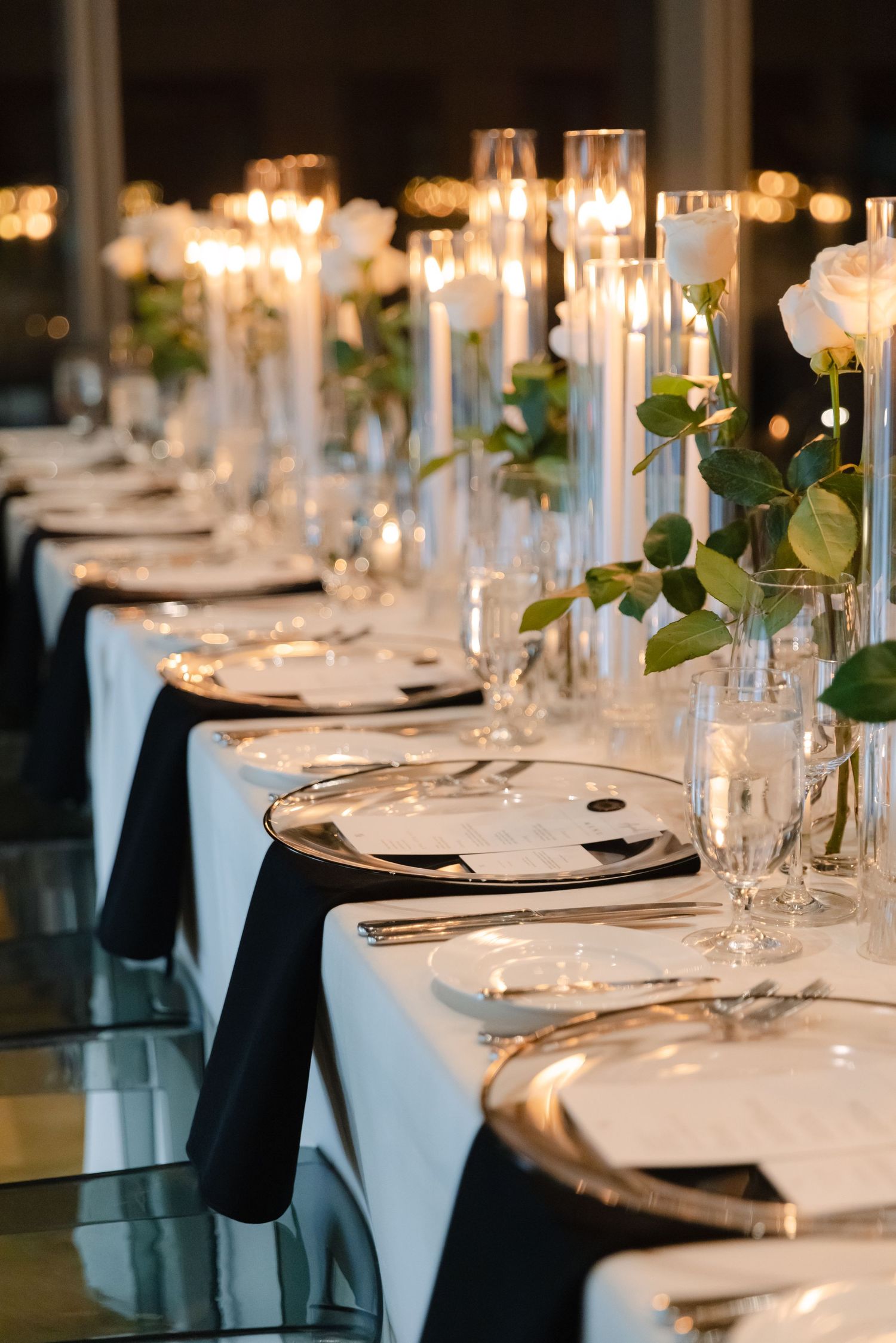 Modern wedding table setting with black napkins, white tablecloths, and tall glass candle holders.