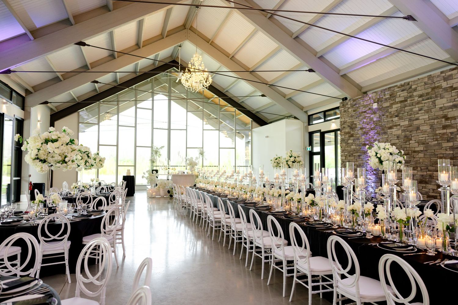 An elegant wedding reception venue with white floral centerpieces and modern white chairs.