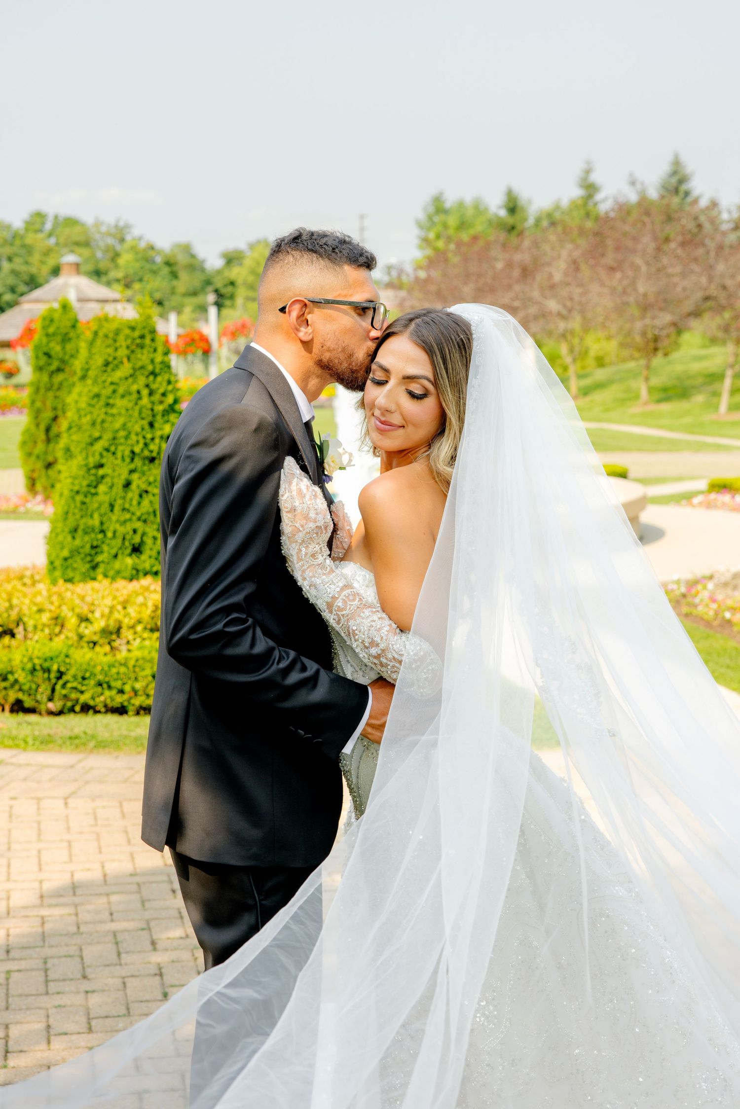 Romantic wedding moment photographed in manicured garden with flowing white veil.