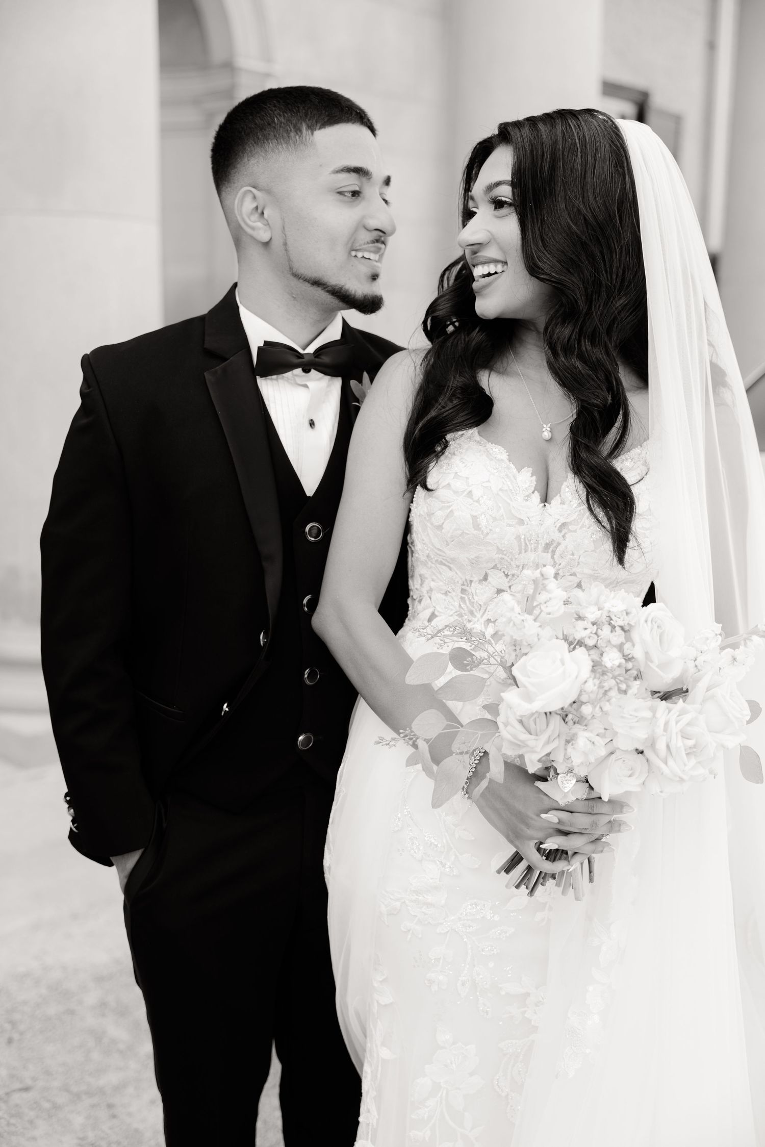 Black and white portrait of newlyweds sharing romantic moment with bride holding bouquet.