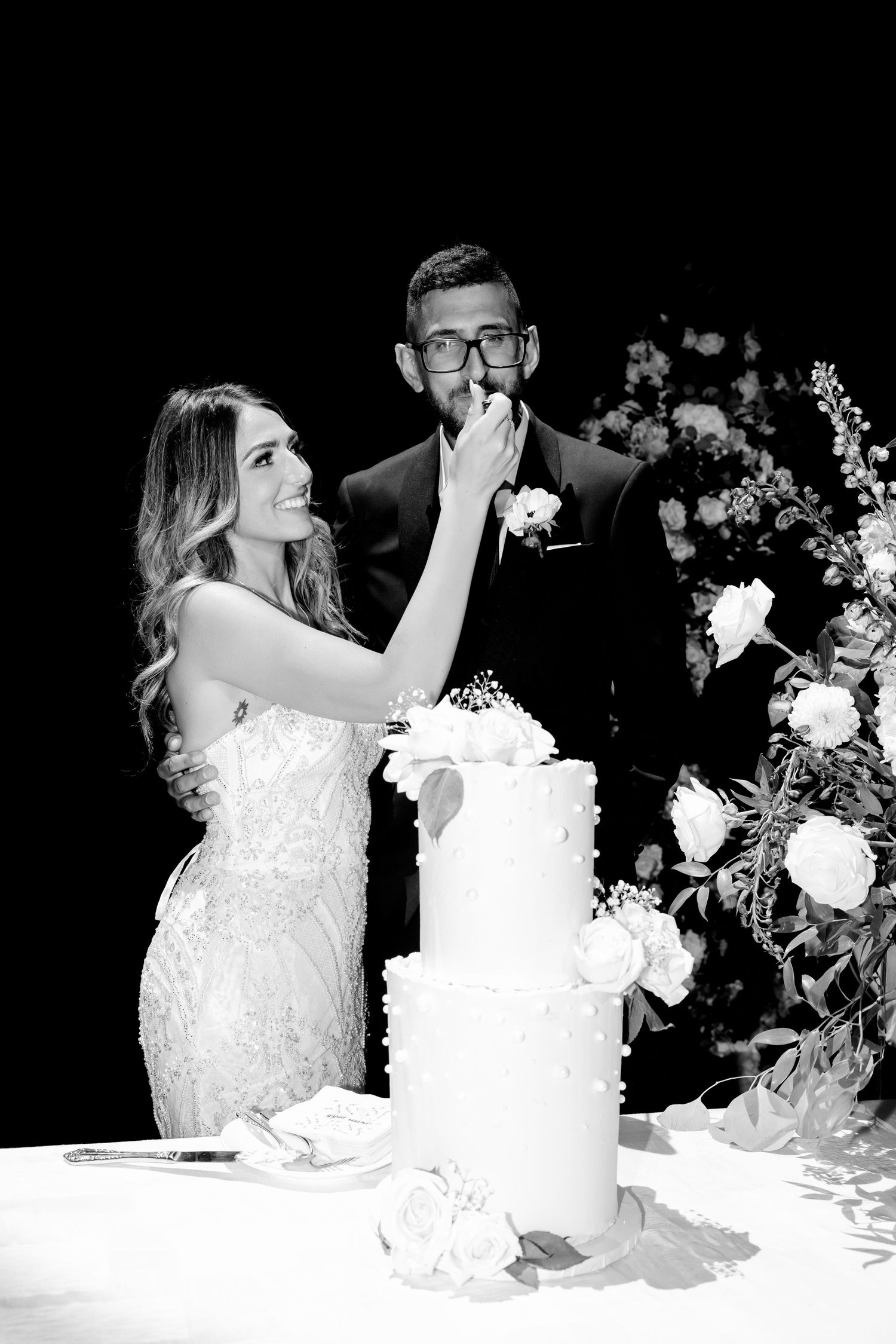 Black and white photo of playful cake feeding moment during wedding reception.