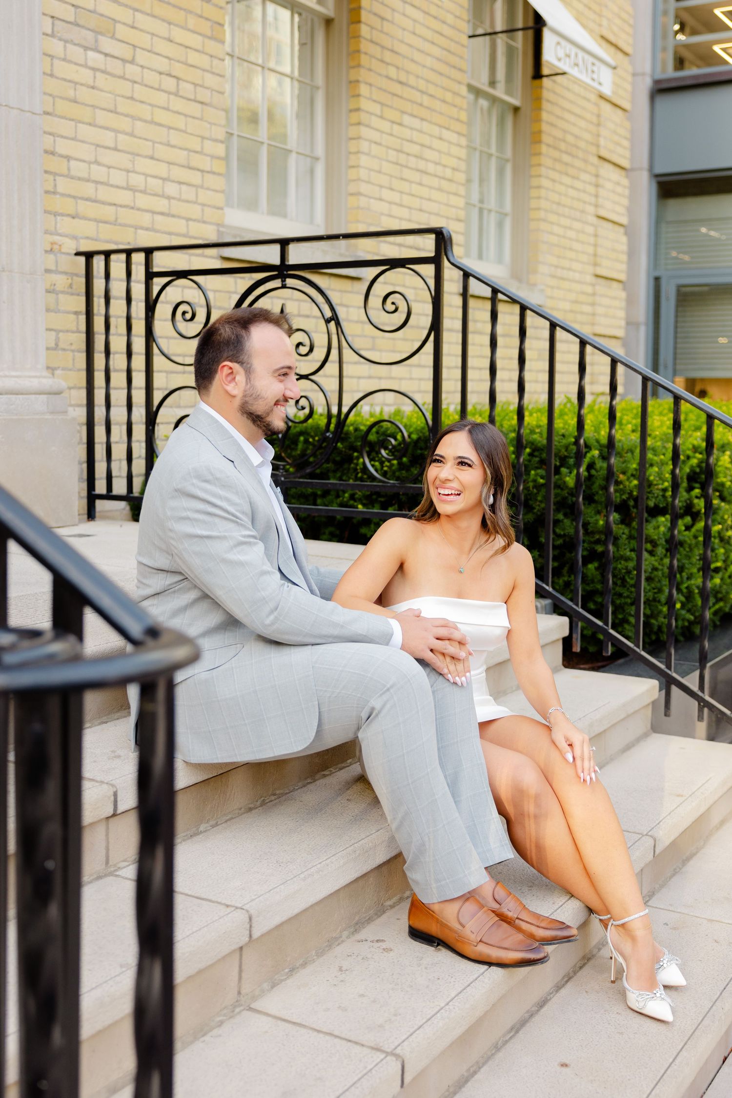A couple shares a tender moment while sitting on the steps of a luxury boutique.