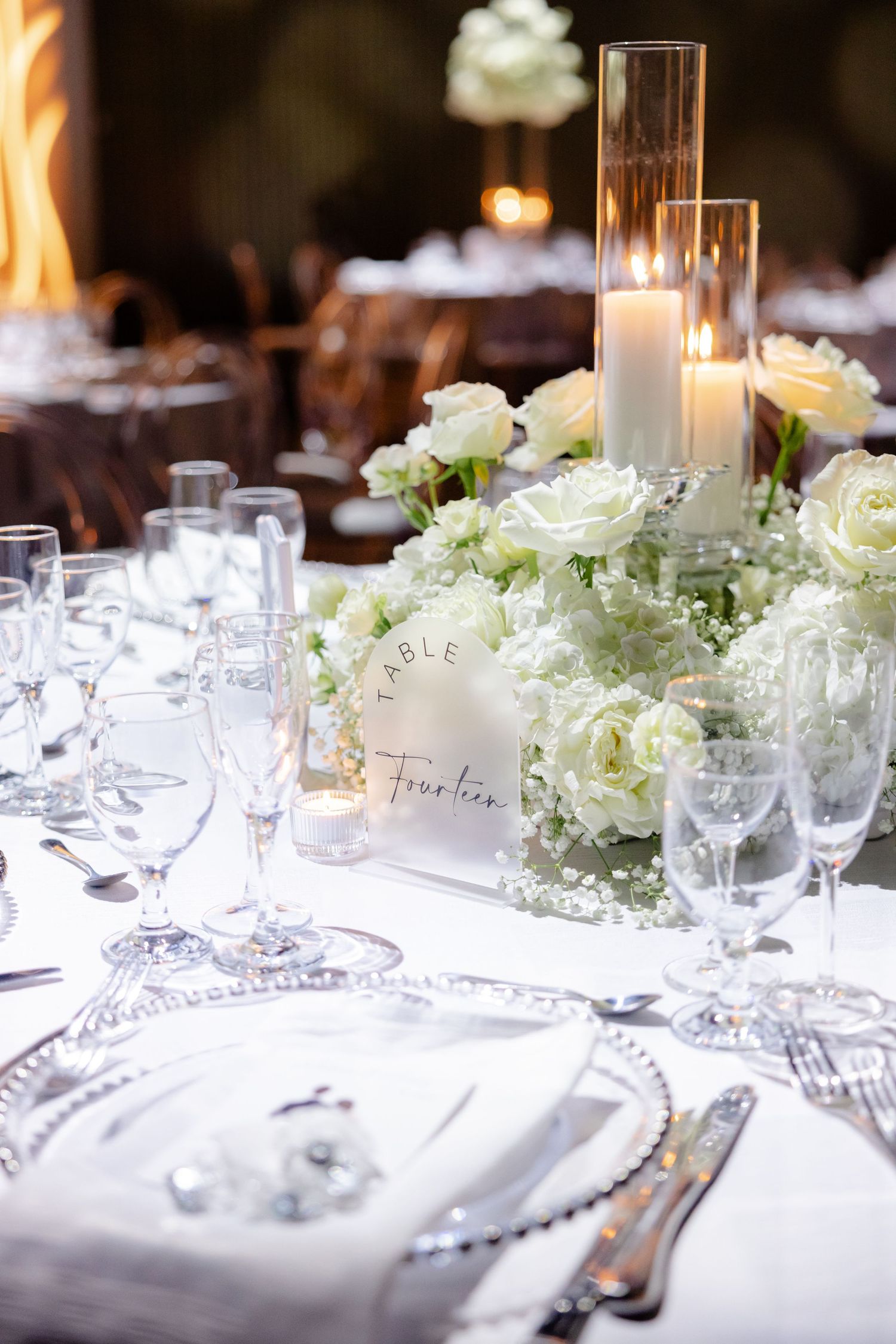Close-up of formal place setting with white roses and glass candleholders on crisp linens.