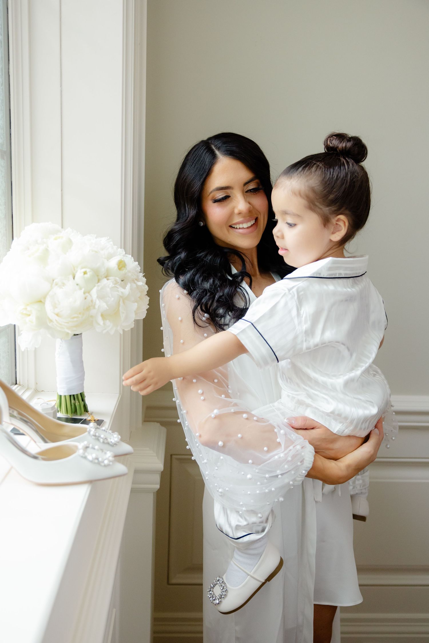 Sweet interaction with a child reaching for white flowers while being held in a light-filled room.