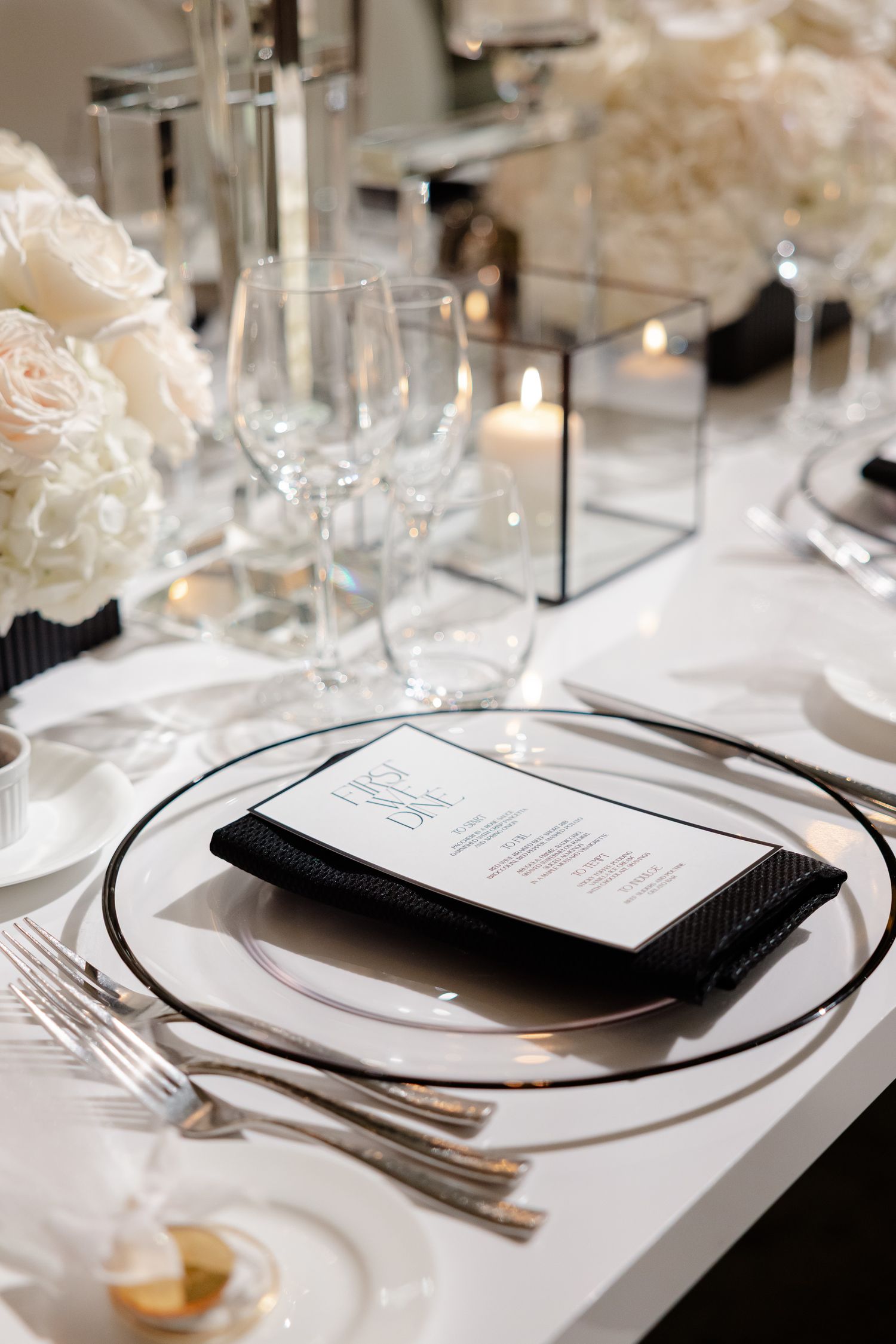 Elegant black and white place settings on a formal dining table with crystal glasses and silver cutlery.