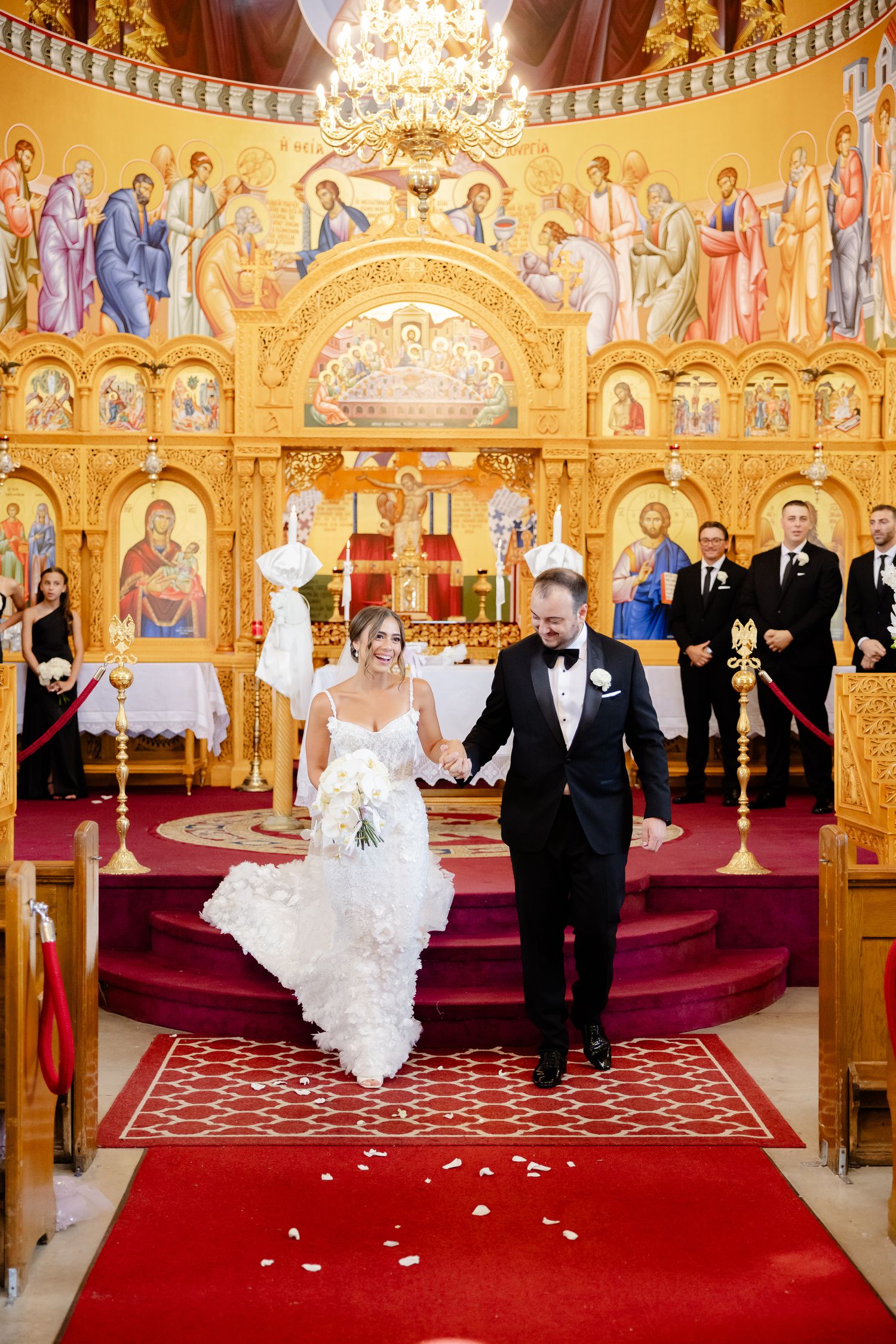 Traditional Orthodox church wedding ceremony in an ornate sanctuary with gilded icons and a red carpet aisle.