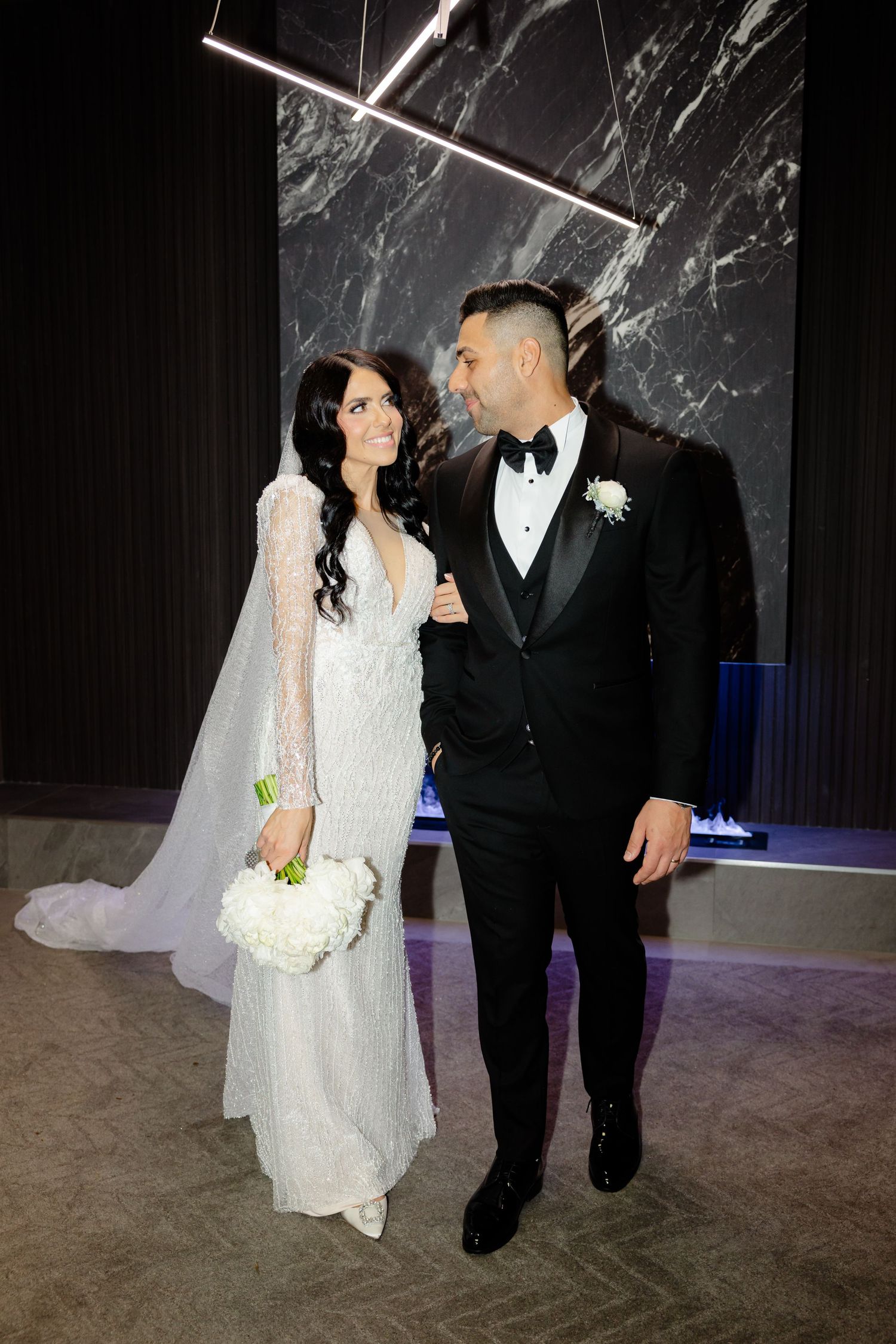 Wedding couple poses in front of dramatic marble wall with modern lighting design.