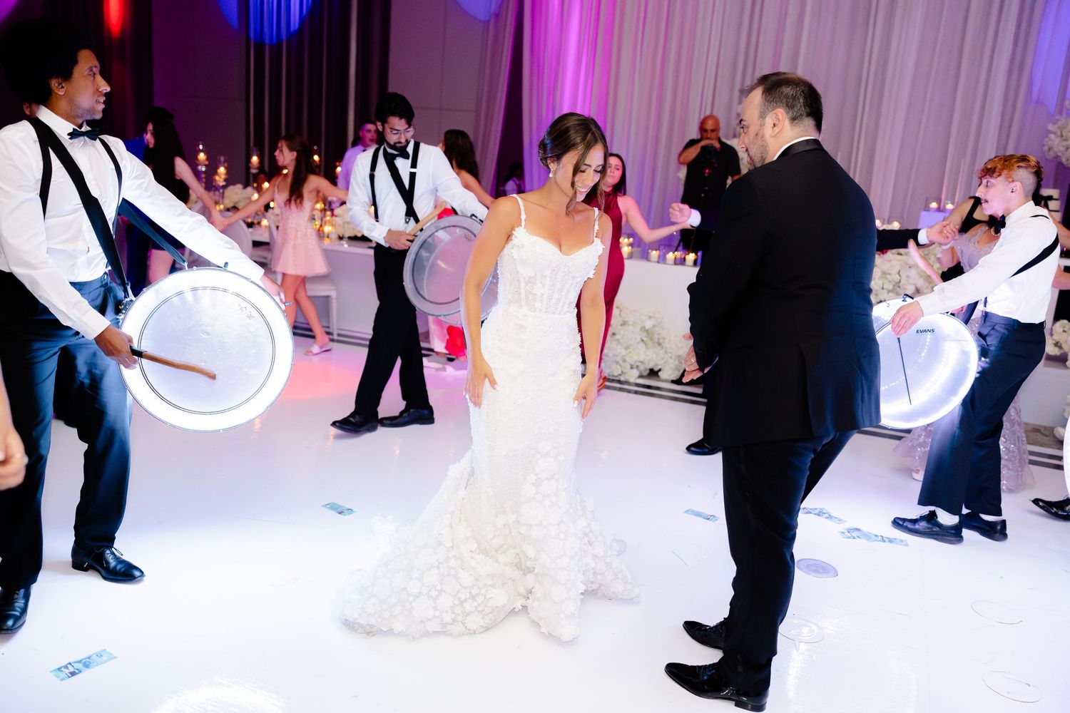 A couple shares a special moment on an illuminated white dance floor at their wedding reception while guests surround them.