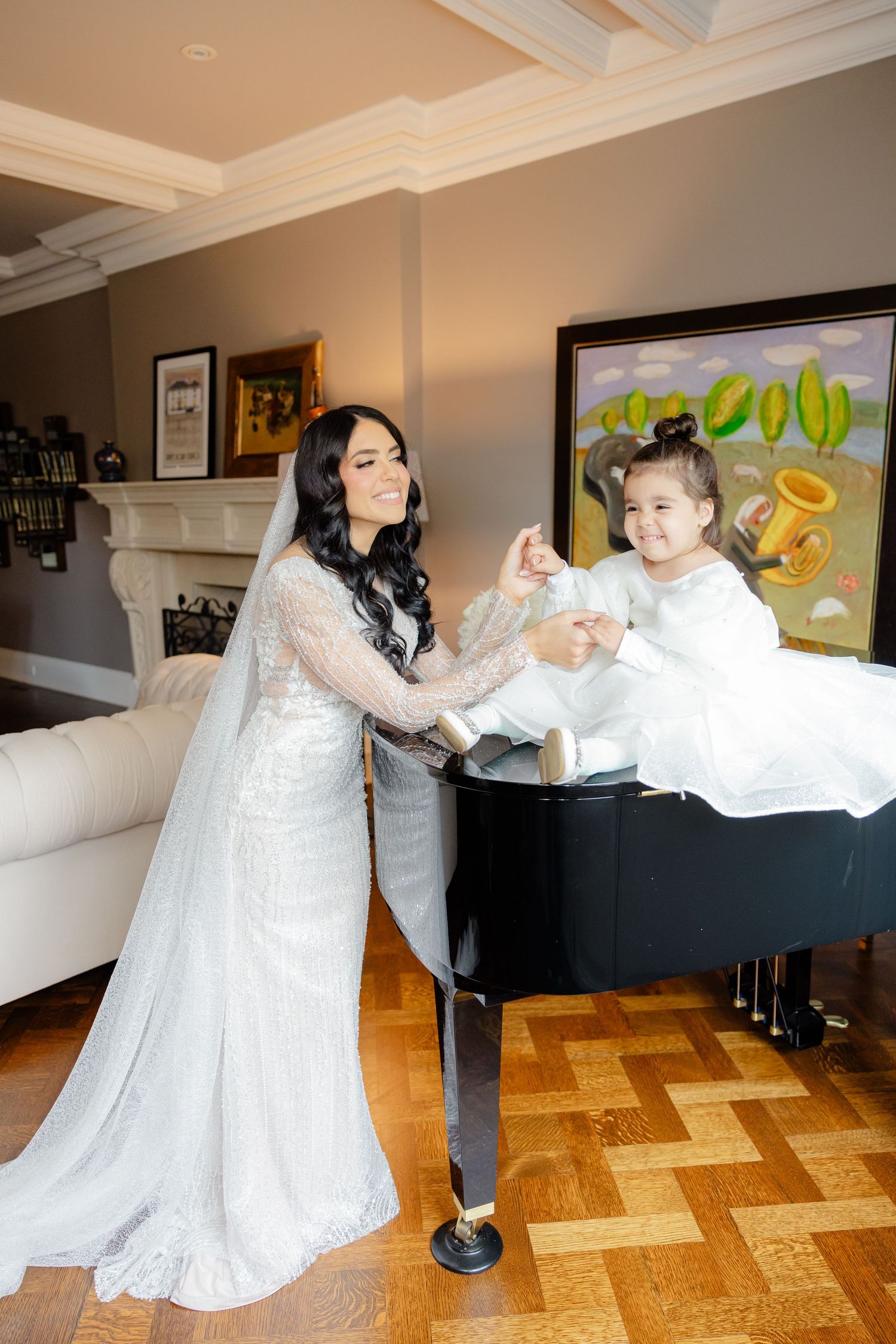 A bride and young attendant share a playful moment on a black grand piano.