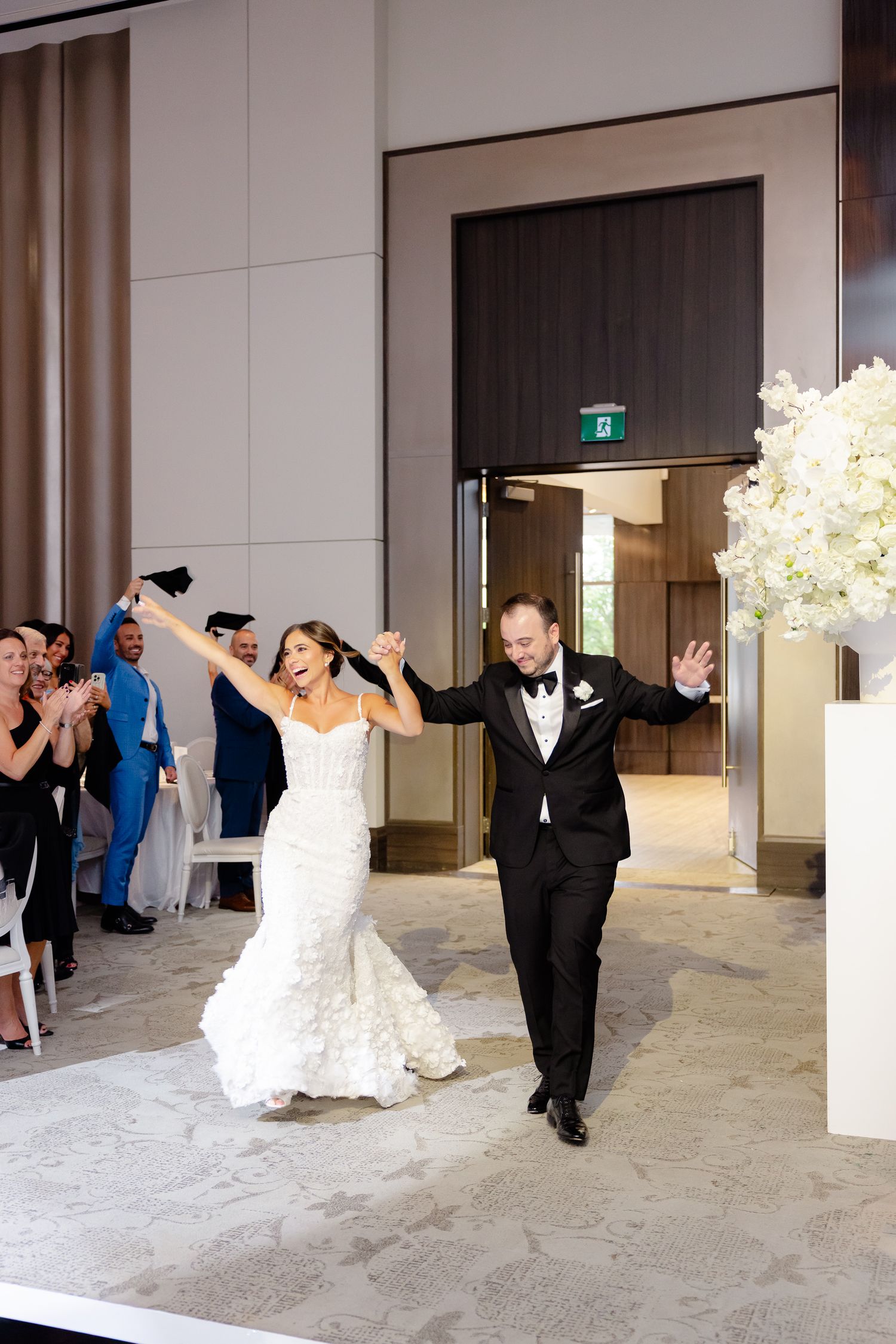 Wedding party members perform a choreographed dance routine in a contemporary venue with white decor.
