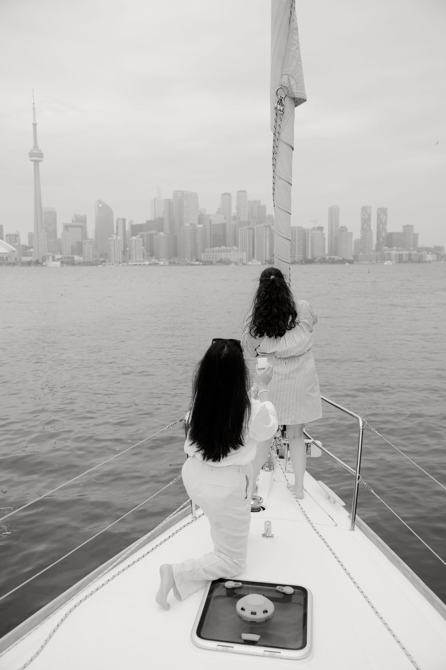 Two people standing on a boat deck overlooking a cityscape with a prominent tower across the water.