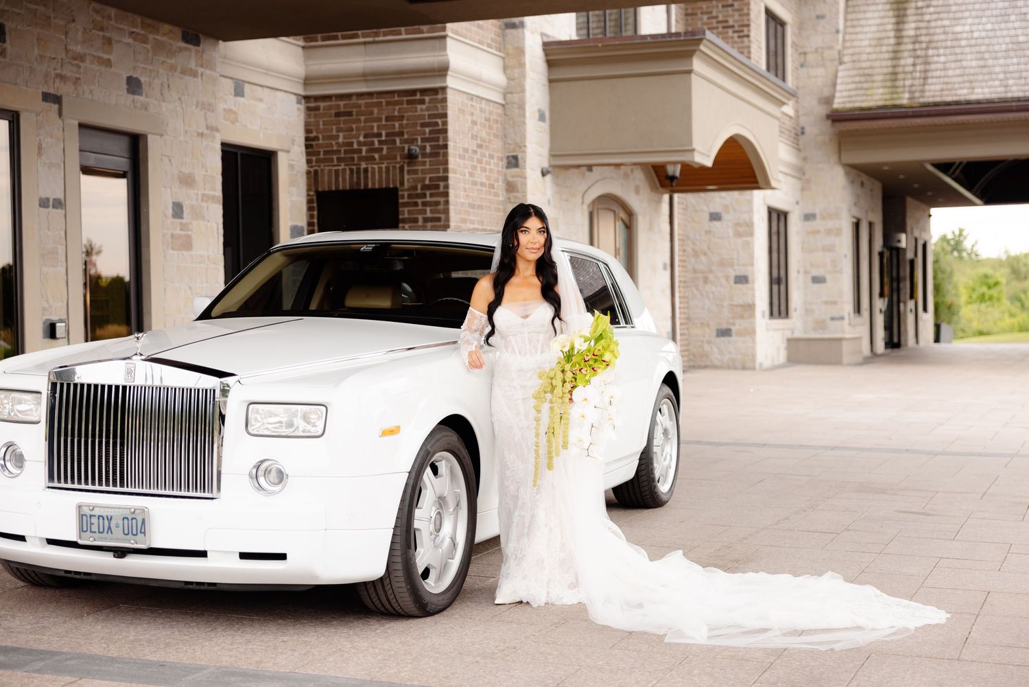 Classic white wedding limousine waiting outside a brick building with elegant archways and columns.