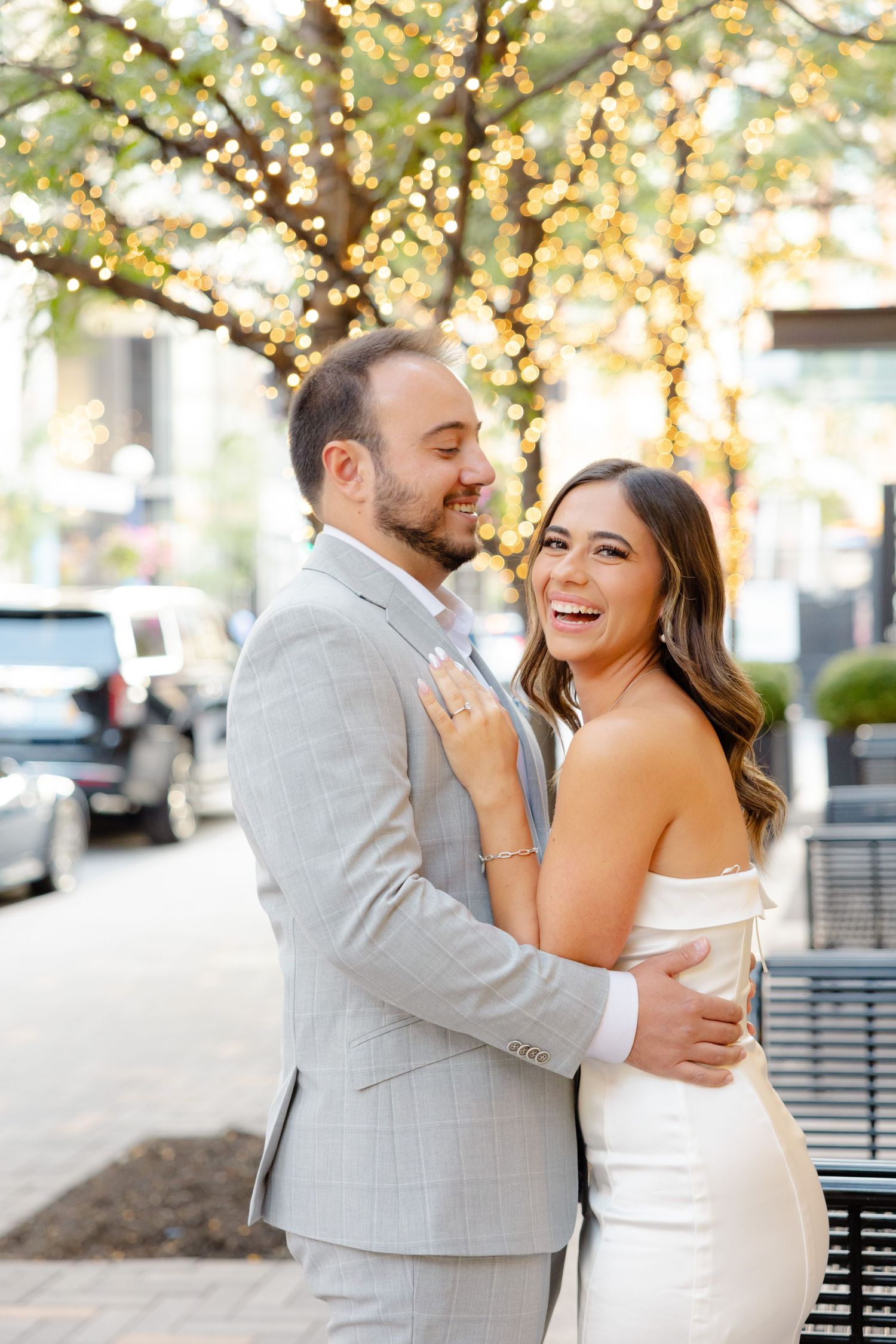 Happy couple shares joyful moment on urban sidewalk with glowing lights in background.