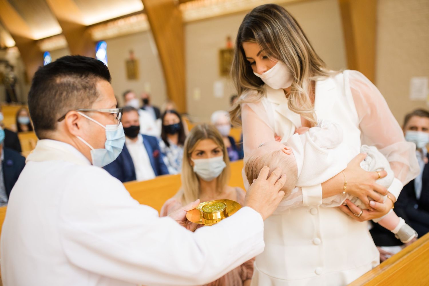 Priest performing blessing during baptism ceremony in church sanctuary.