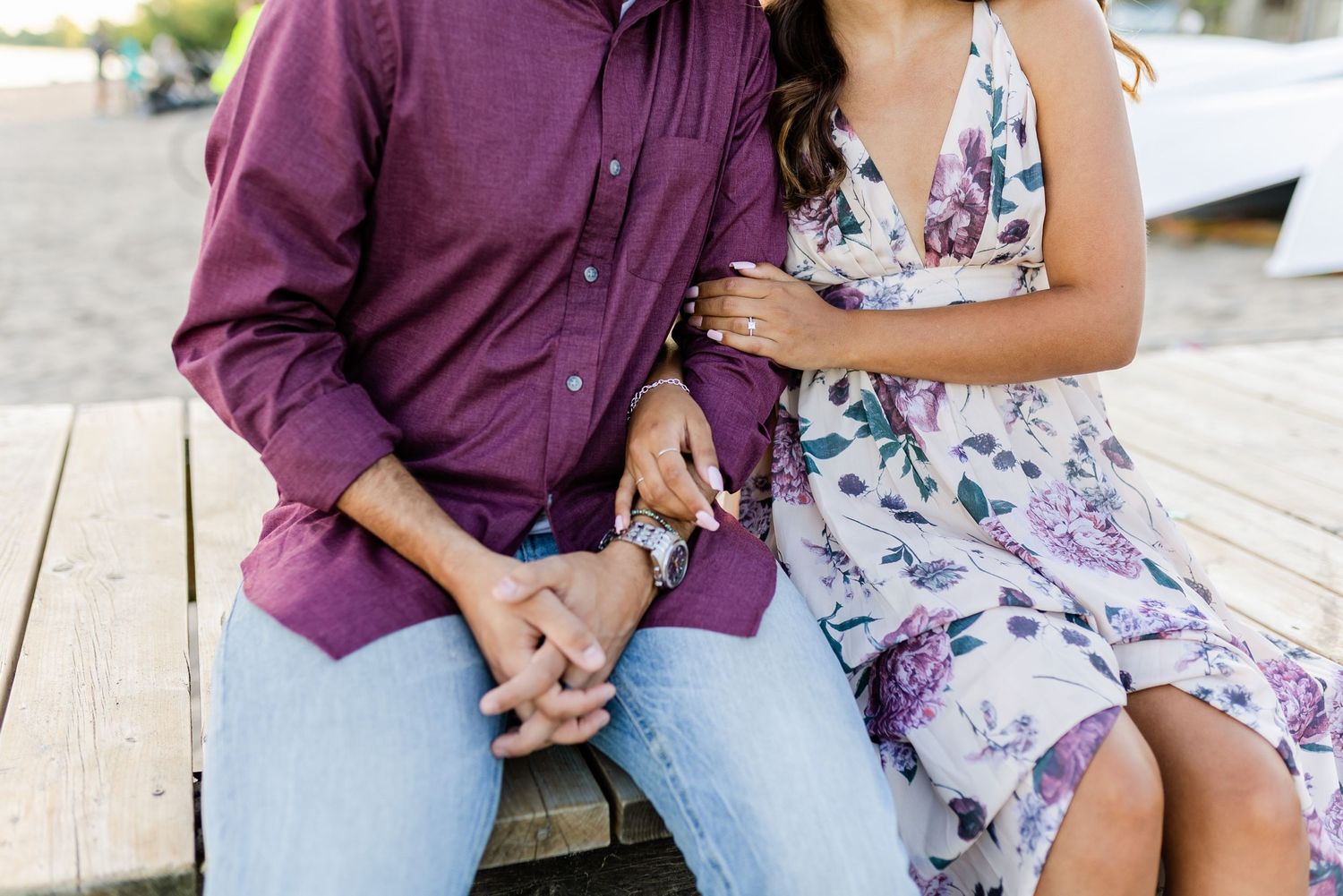 Close up of couple sitting together on wooden dock near the water.