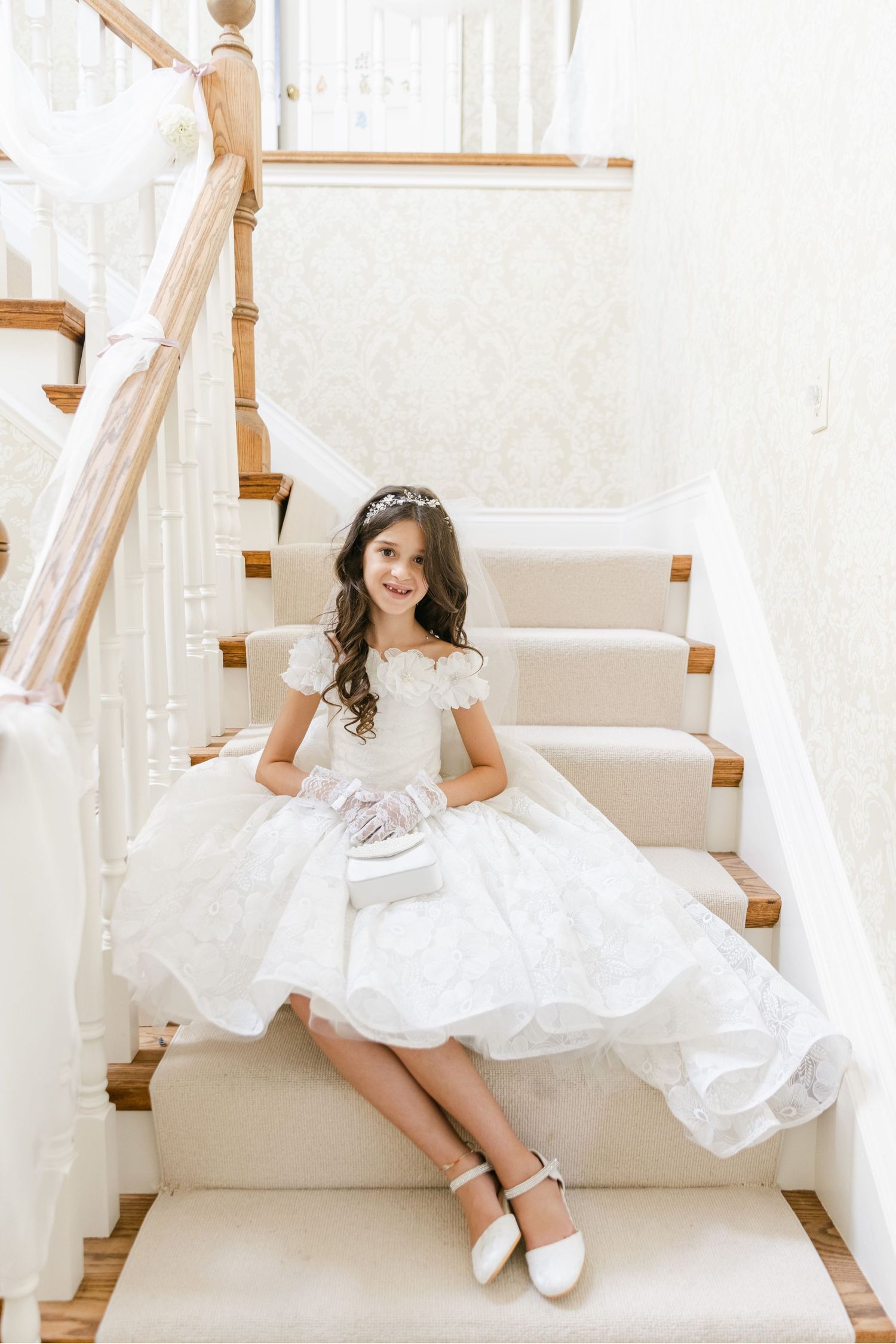 White communion dress with lace details shown on carpeted stairs.
