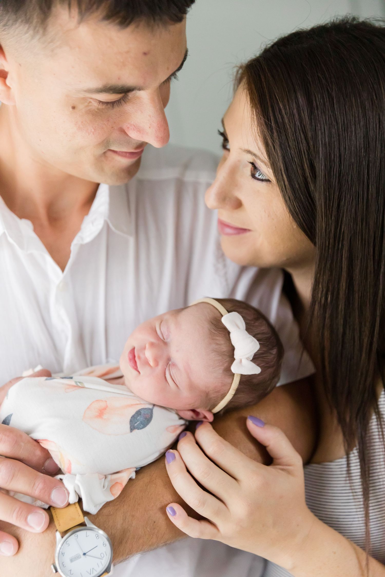 Parents share an intimate moment while holding their sleeping newborn in a patterned blanket.