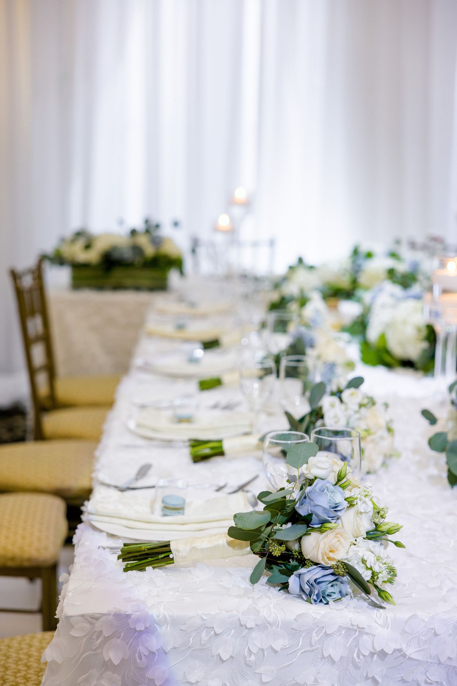 Detailed view of wedding table with white floral arrangements and place settings on textured tablecloth.
