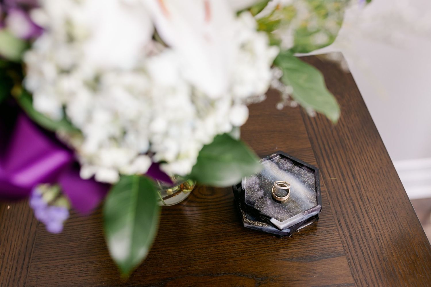 Wedding ring displayed on geometric gray ring holder next to floral arrangement.