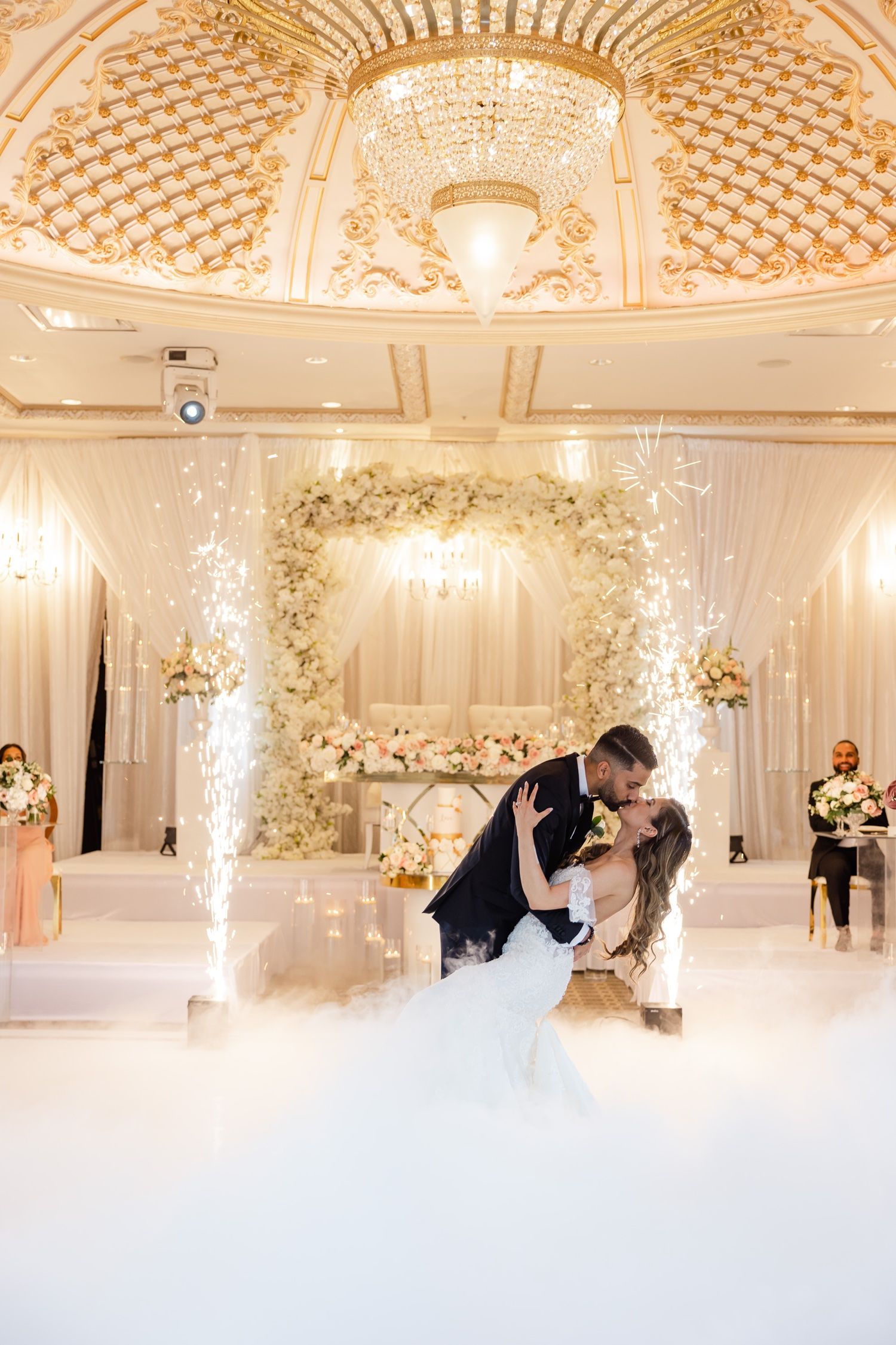 Newlyweds share their first dance under an ornate chandelier with fog and pyrotechnics.