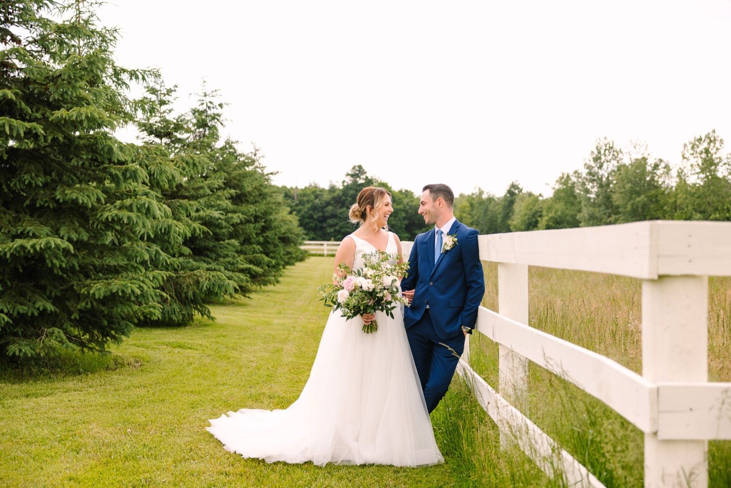 Beautiful outdoor wedding portrait with white fence and evergreen backdrop.