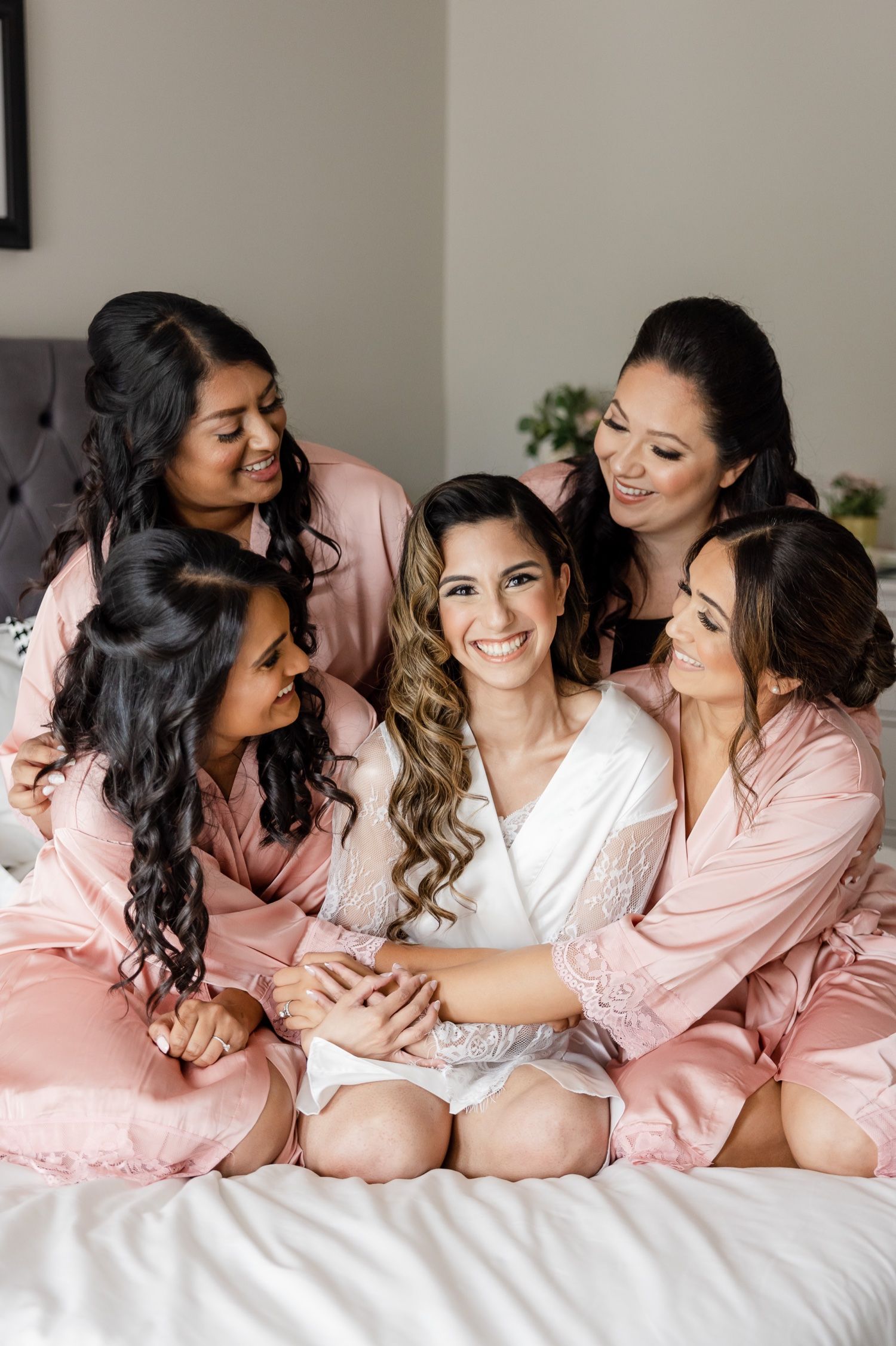 Intimate wedding morning scene with bridesmaids in pink robes gathered on bed.