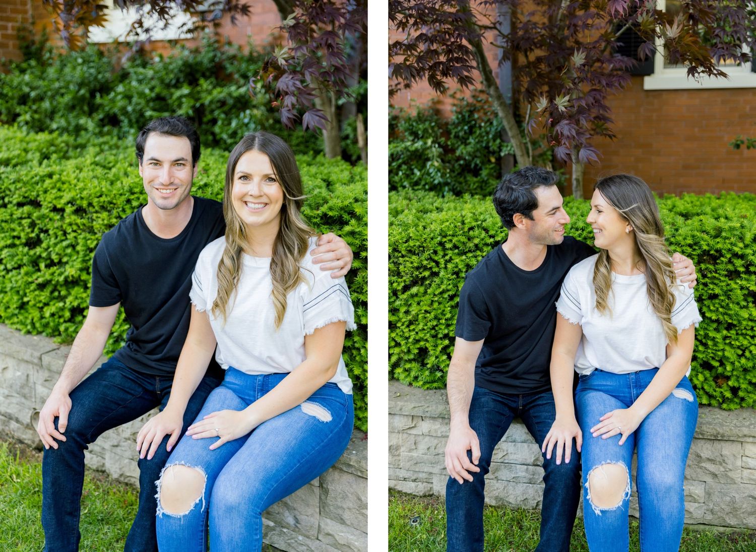 A couple sits casually together on a stone wall with brick building and greenery in background.