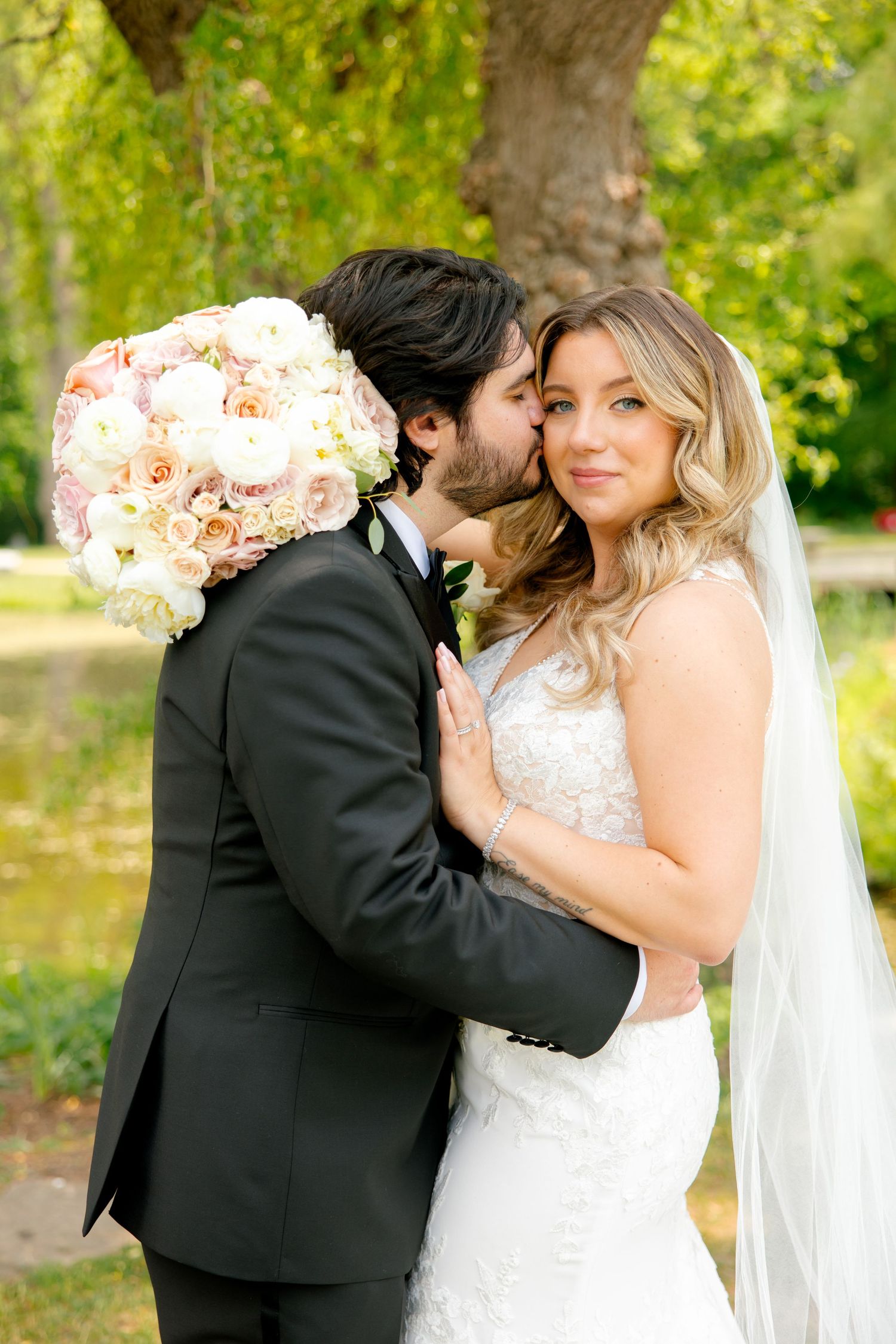 Intimate wedding portrait under willow tree with bride holding blush pink floral bouquet.