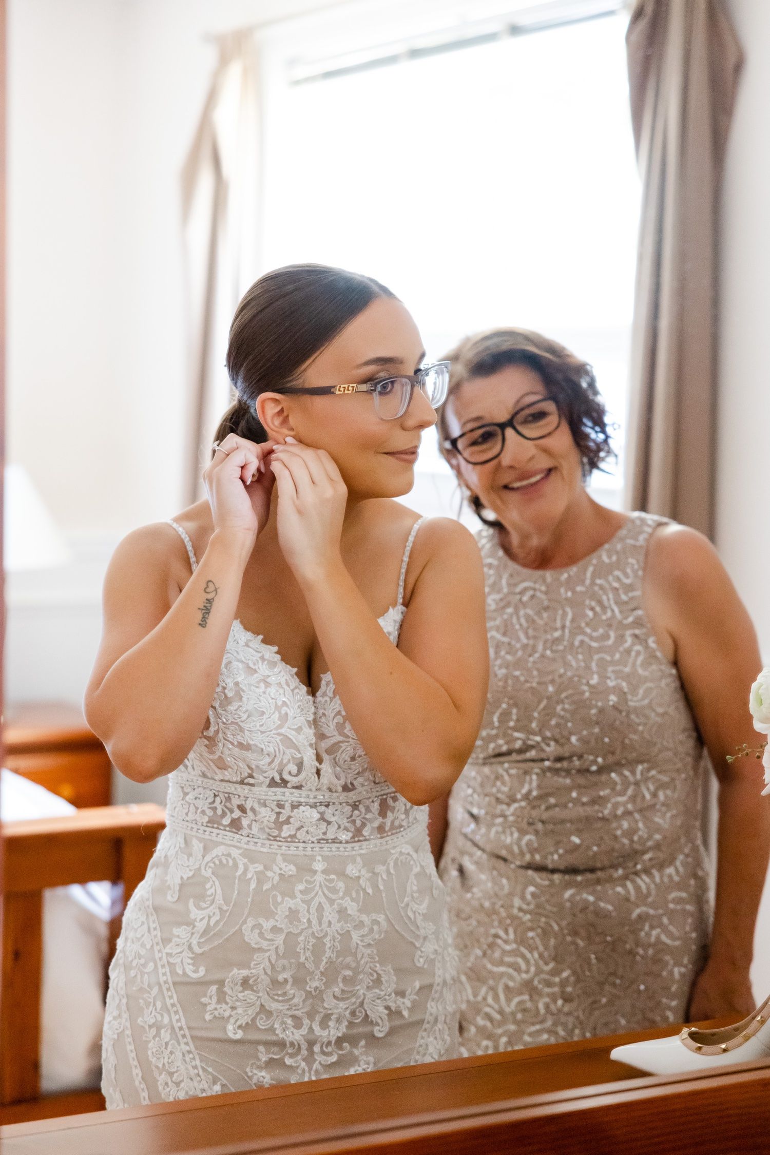 A touching getting ready moment captured in front of a window with soft natural light.