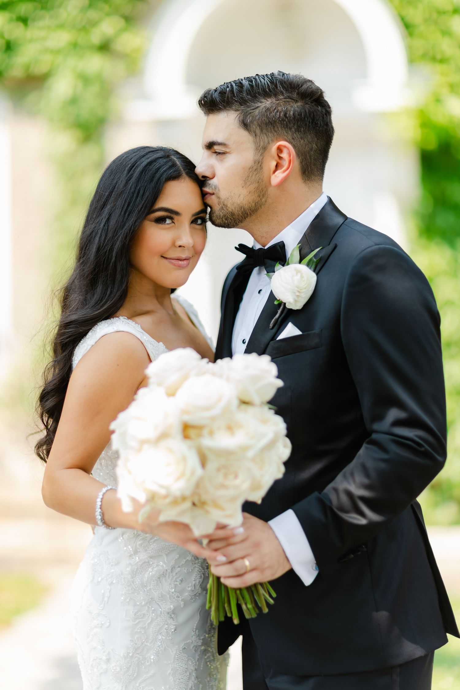 Intimate wedding portrait of couple sharing tender moment with white rose bouquet.