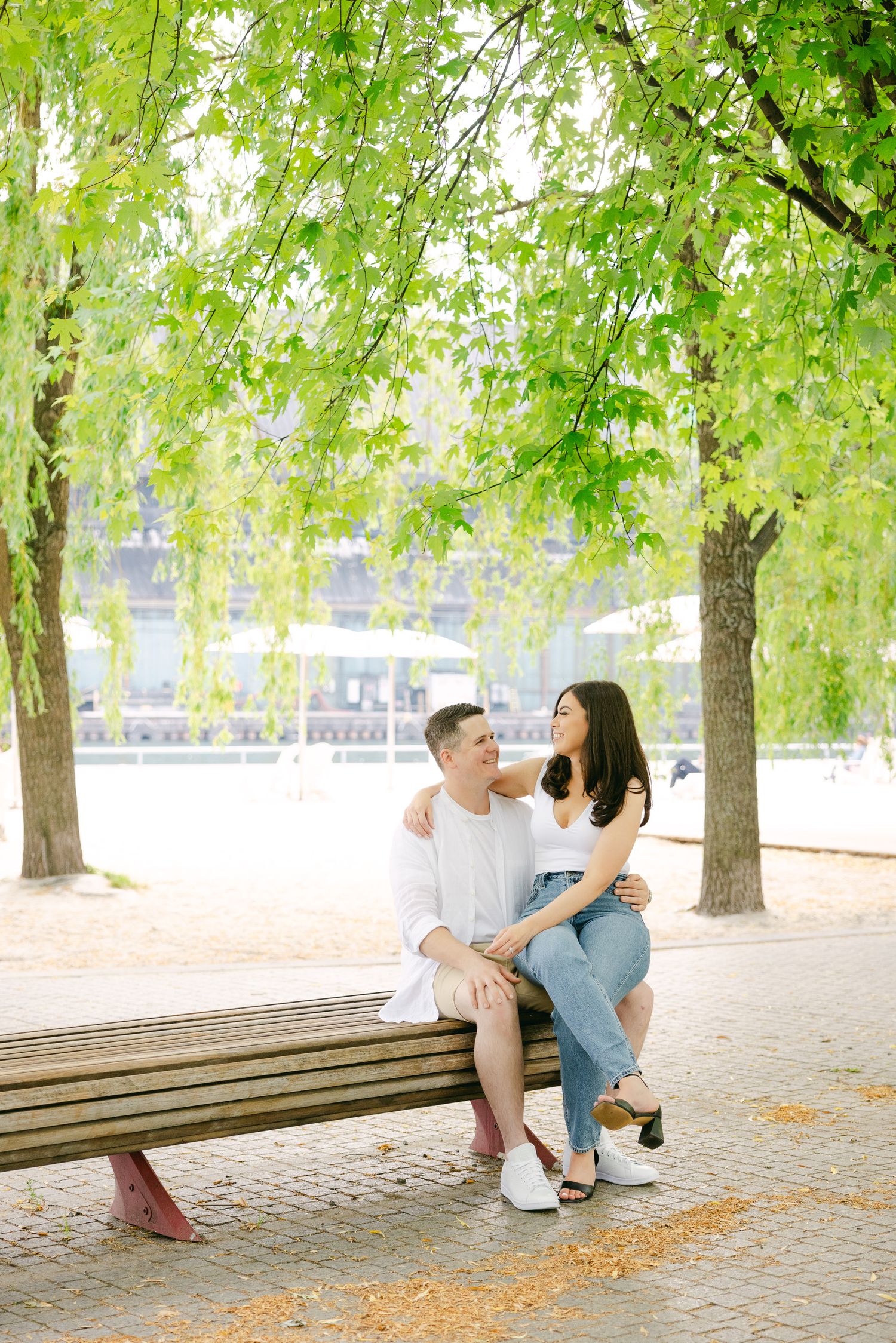 A sunny outdoor portrait of a couple sitting together on a park bench under willow trees.