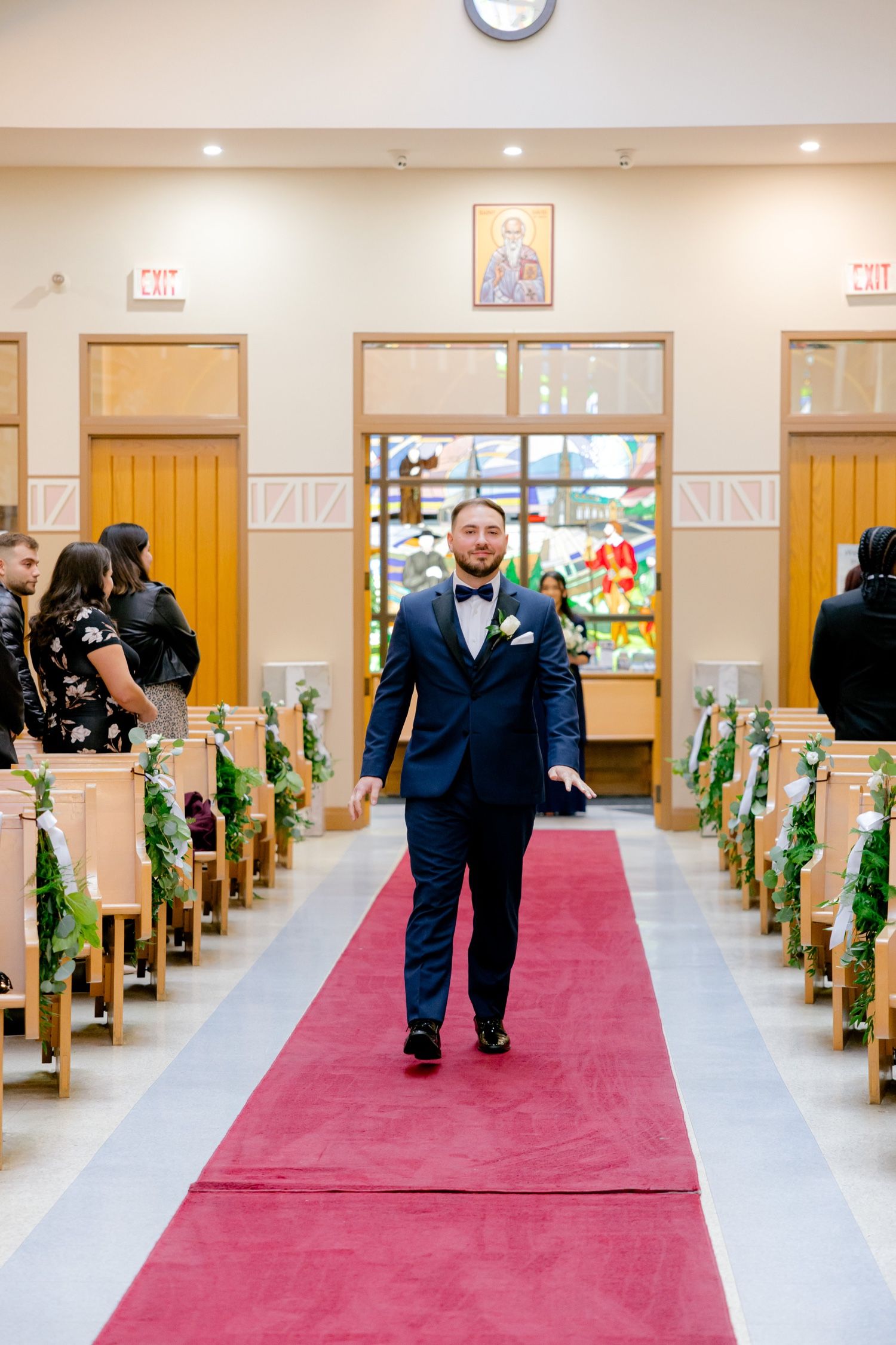 Wedding ceremony aisle with red carpet and wooden pews decorated with greenery.
