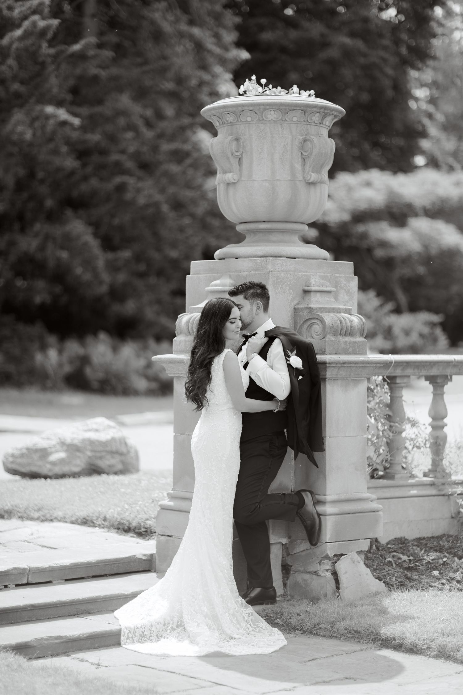 Black and white photo of newlyweds sharing an intimate moment beside a decorative stone pillar.