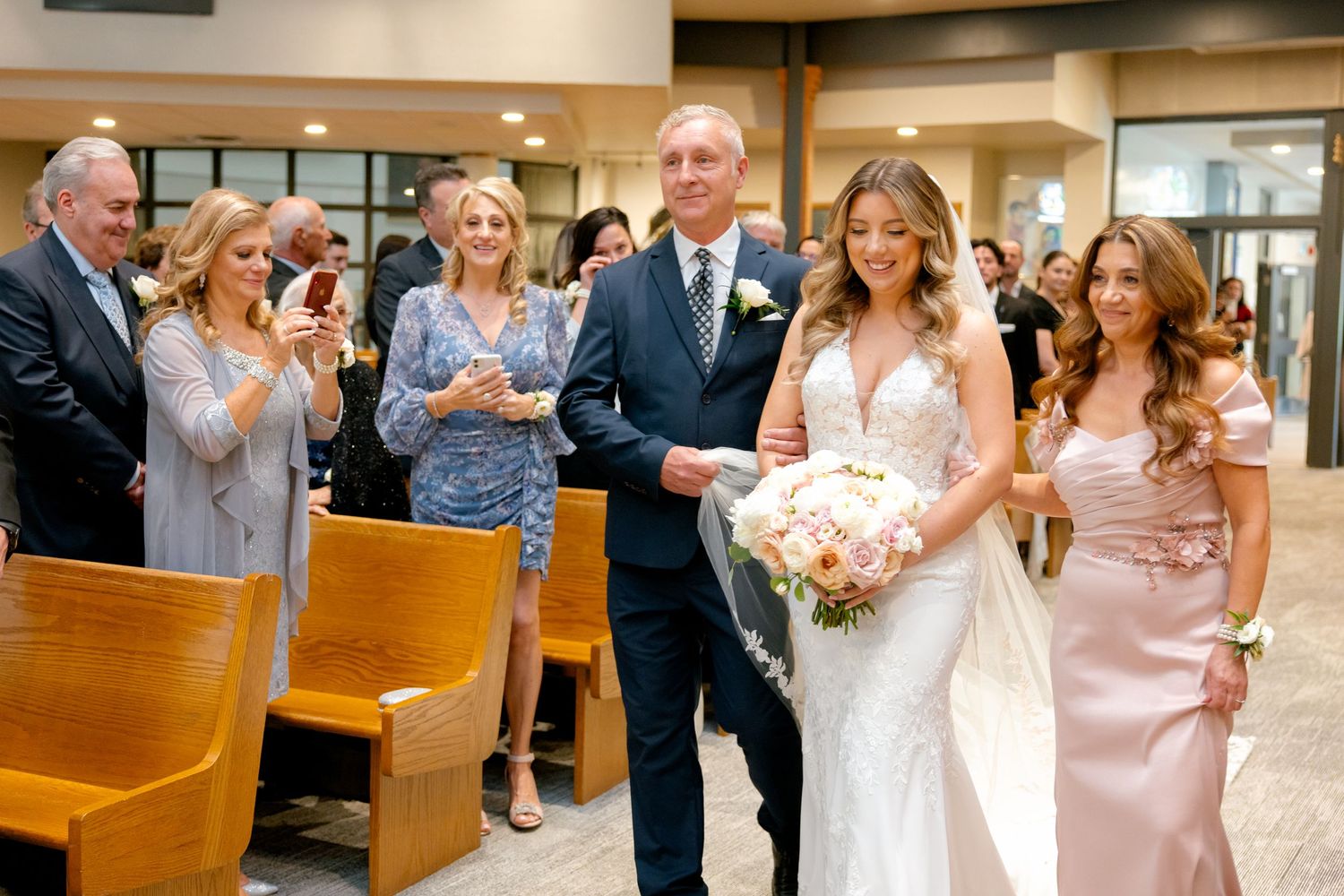 Wedding ceremony in modern church with guests watching processional from wooden pews.