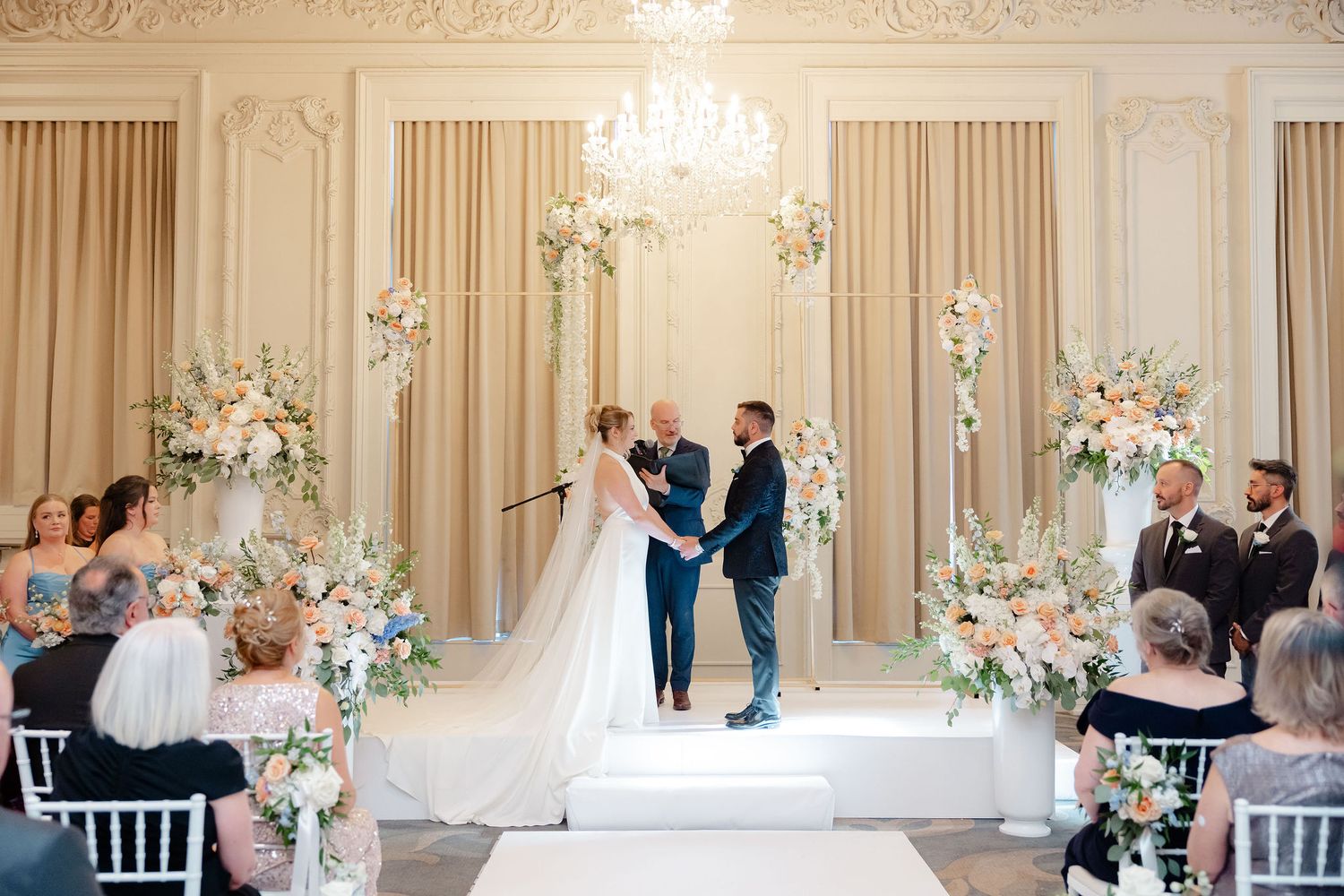 Panoramic view of an elegant wedding ceremony setup with floral arrangements and white chairs in a classic ballroom.
