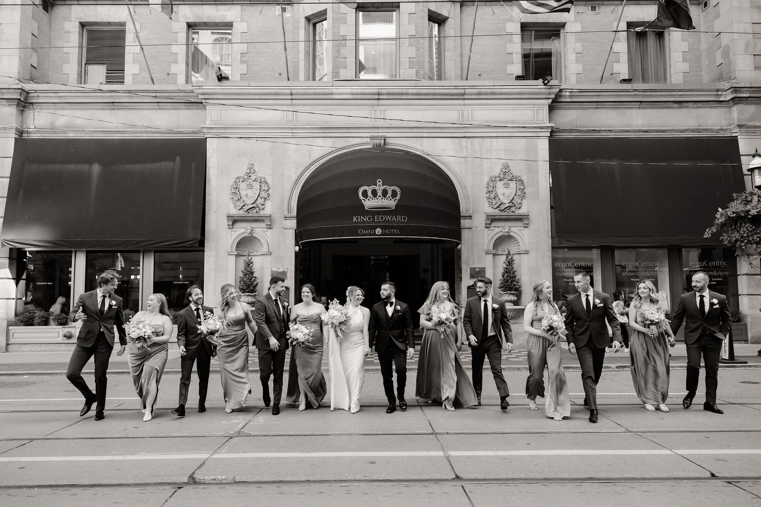 A black and white panoramic shot of wedding guests lined up outside a building.