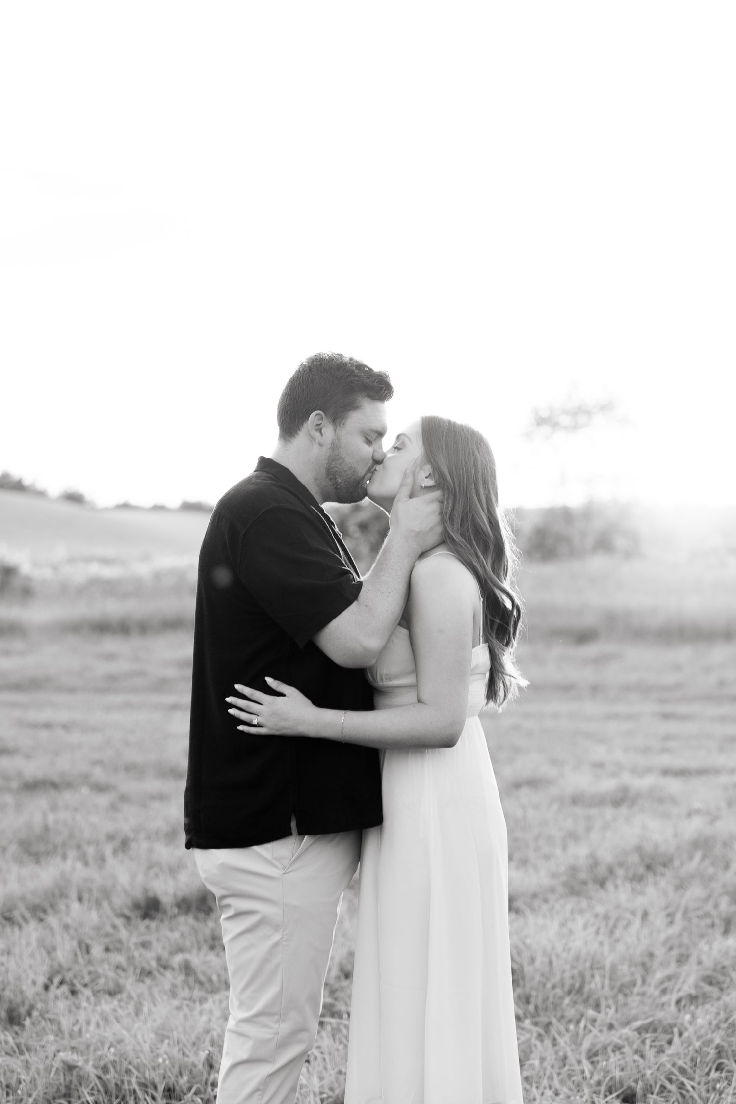 Black and white romantic portrait of couple about to kiss in open field.