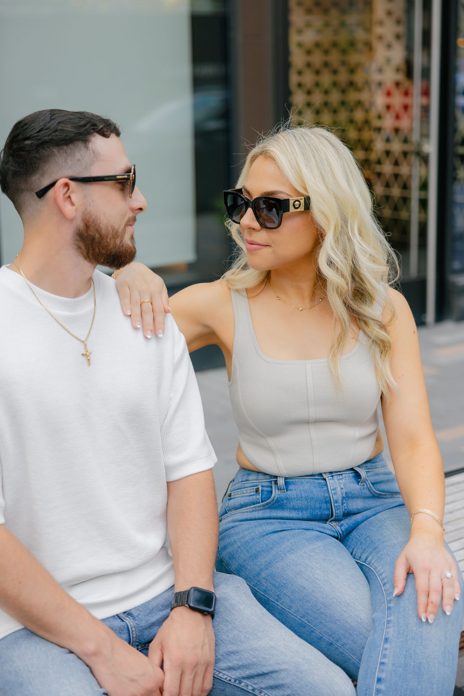Stylish couple in sunglasses sitting together wearing casual outfits of white t-shirt, tank top and jeans.