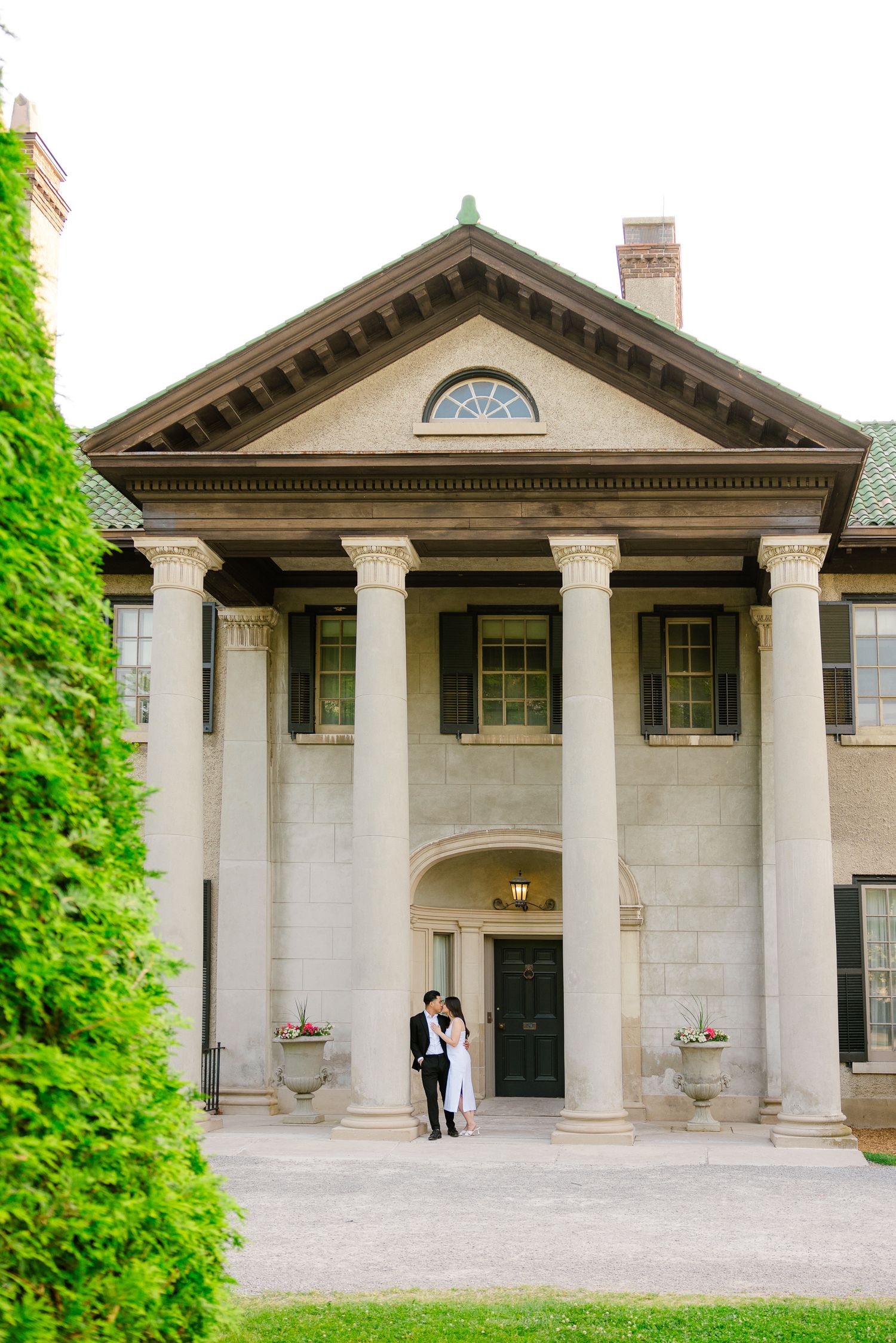 Majestic stone mansion entrance with classical columns and formal couple at doorway.