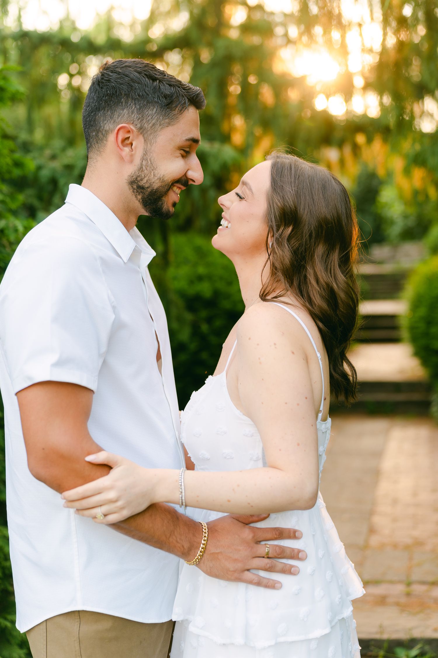 Couple shares an intimate moment while laughing together in a sunlit garden pathway.