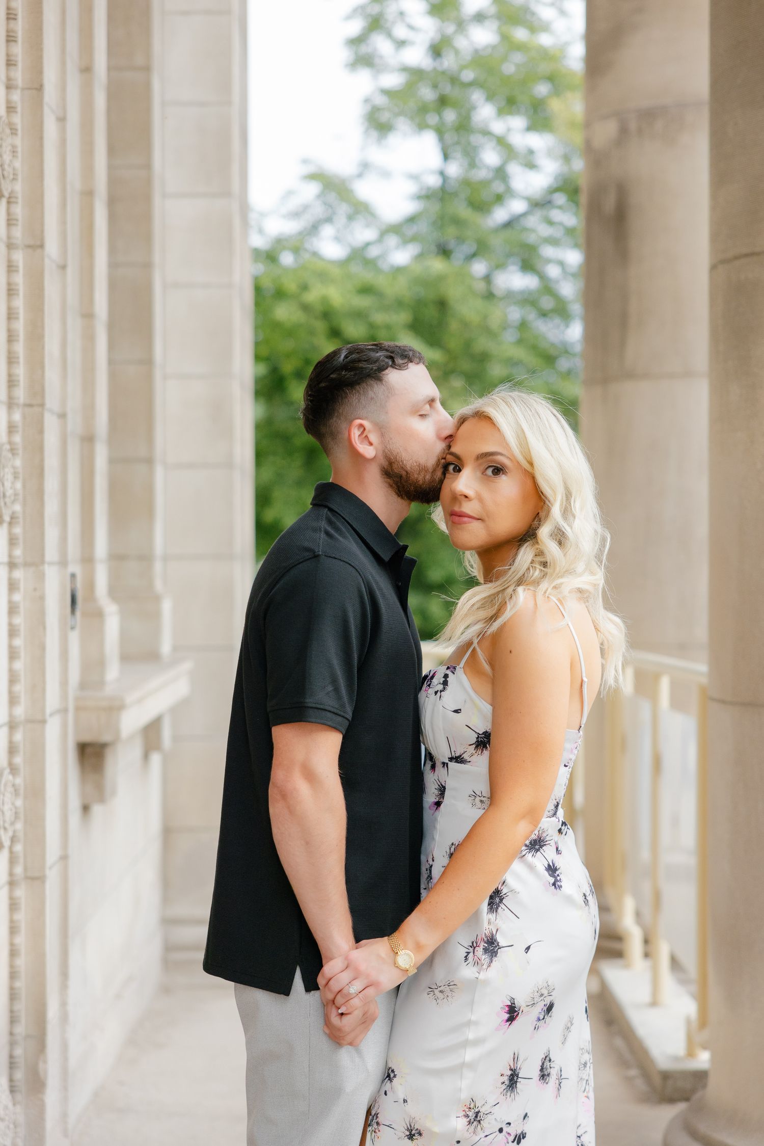 Couple dressed in black and floral white embraces between classic architectural columns.