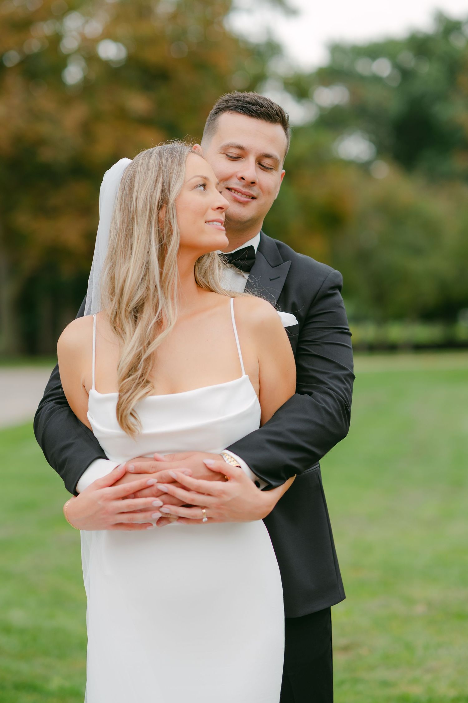 Romantic wedding couple embraces in an outdoor garden setting.