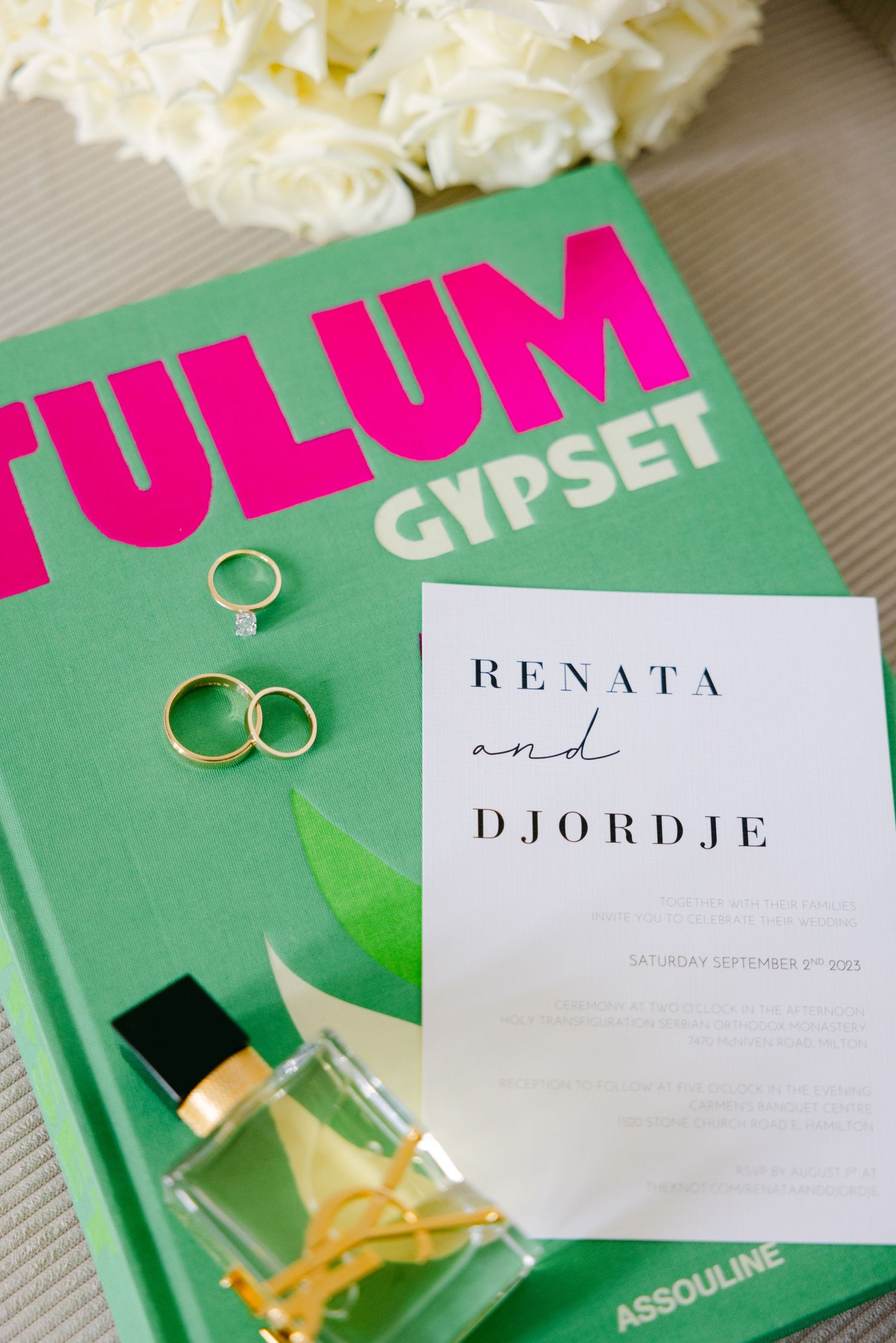Wedding invitation and rings displayed on green Tulum coffee table book with white flowers.